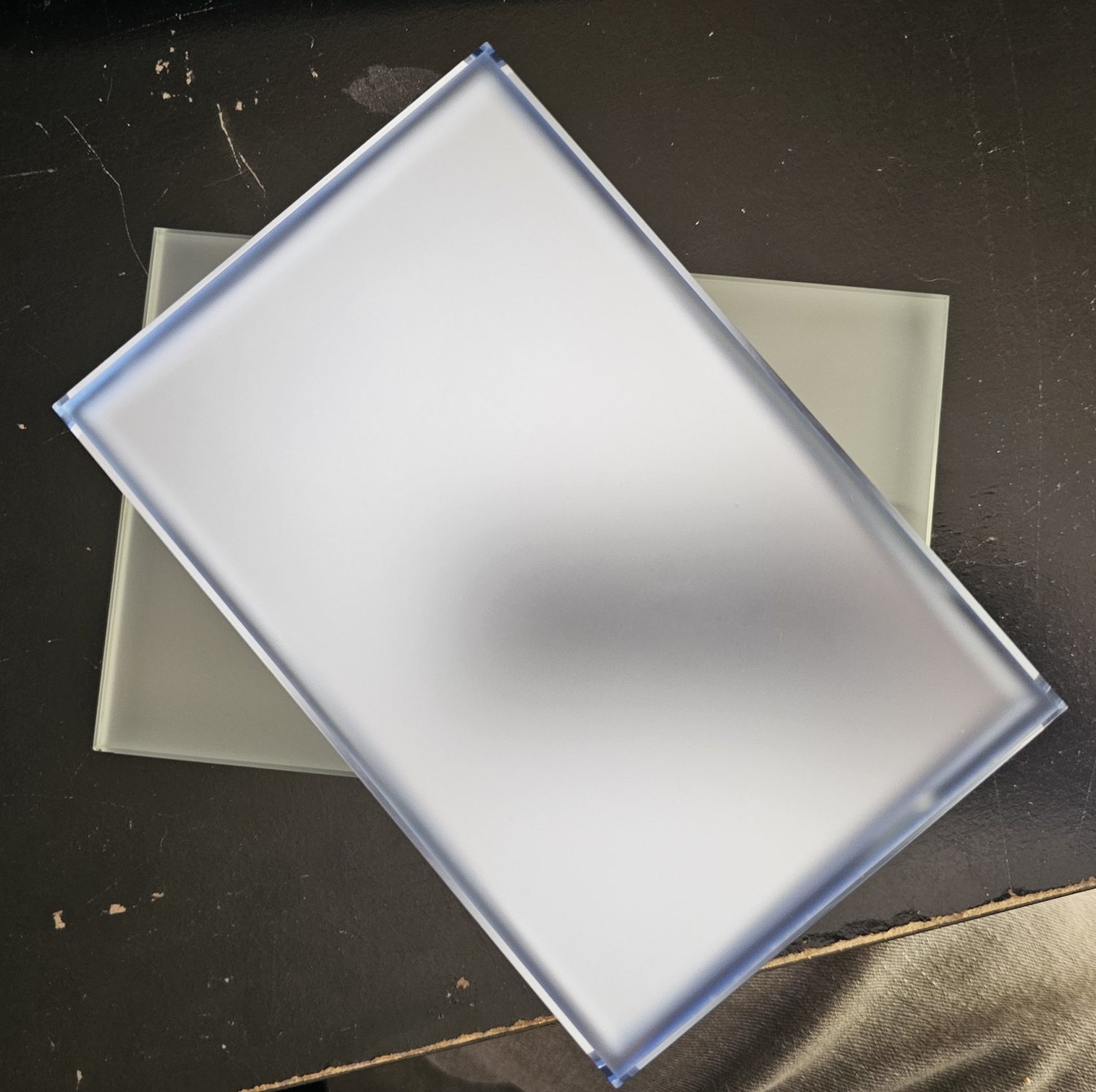Blue laminated glass sample lying across a clear frosted glass sample, seen from above