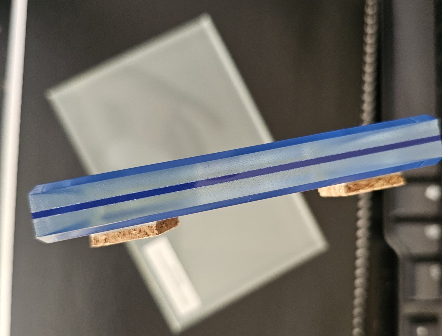 Edge of a blue glass sample showing two lites bonded together, a blue mirror at the back and velour-finished blue glass in front