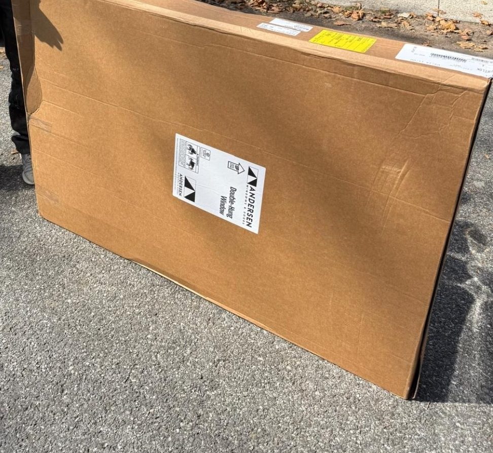 Andersen double-hung window delivered in its own individual cardboard carton, labeled, standing on the street before being carried to the opening