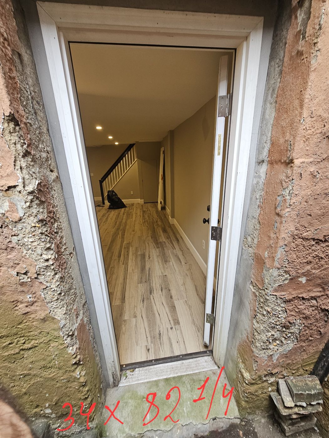Existing exterior door opening in a stucco wall, marked 34 by 82 and a quarter inches