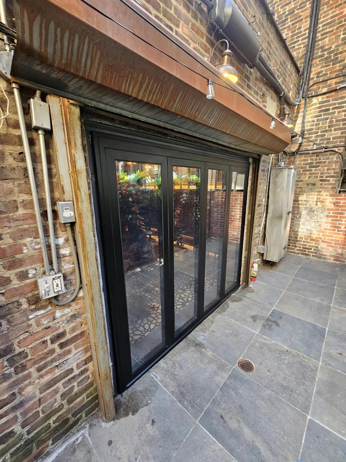 Black thermally broken aluminum bifold door closed, seen from the back patio of a restaurant at 107 1st Avenue, East Village, Manhattan