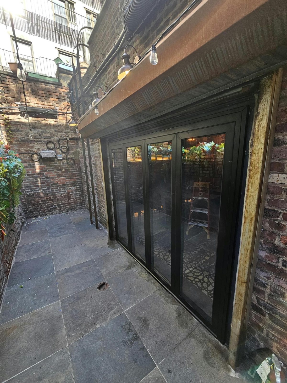 Restaurant patio at 107 1st Avenue, East Village, Manhattan, with the new black aluminum bifold door along the brick wall