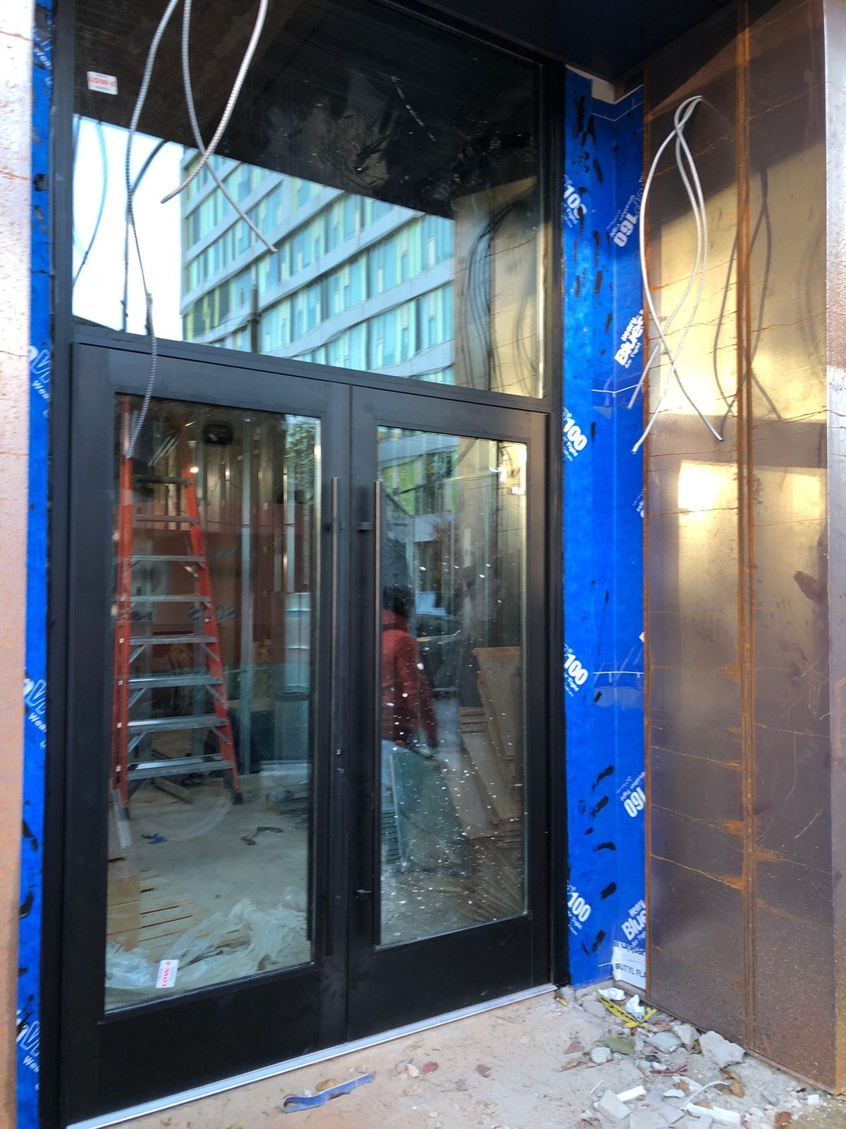Pair of black aluminium storefront doors with full-height ladder pulls and a glazed transom above, set in a membrane-flashed opening beside weathering-steel cladding at 1209 Vine Street, Philadelphia