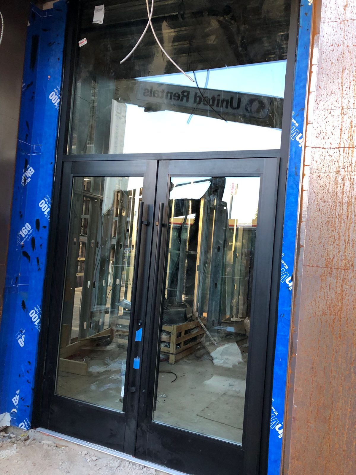 Black aluminium storefront double doors with a tall transom and low-E glass labels at the ground floor of 1209 Vine Street, Callowhill, Philadelphia, during construction