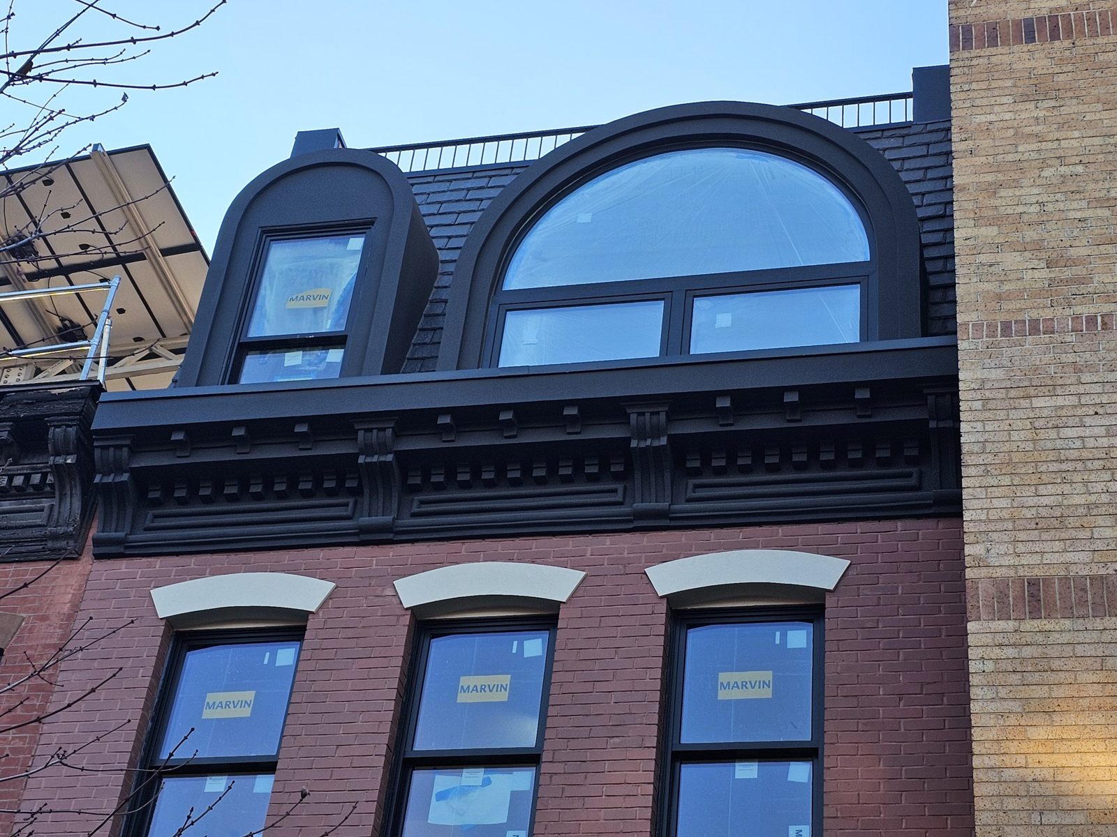 Arched aluminium dormer window with a fixed arched top lite and two in-swing casements below, beside a smaller dormer with a Marvin double-hung, above the cornice at 126 Washington Avenue, Clinton Hill