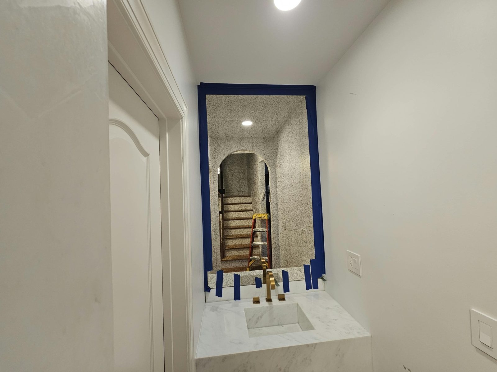 Antique mirror filling the niche above a marble sink in a Borough Park powder room, seen from the doorway