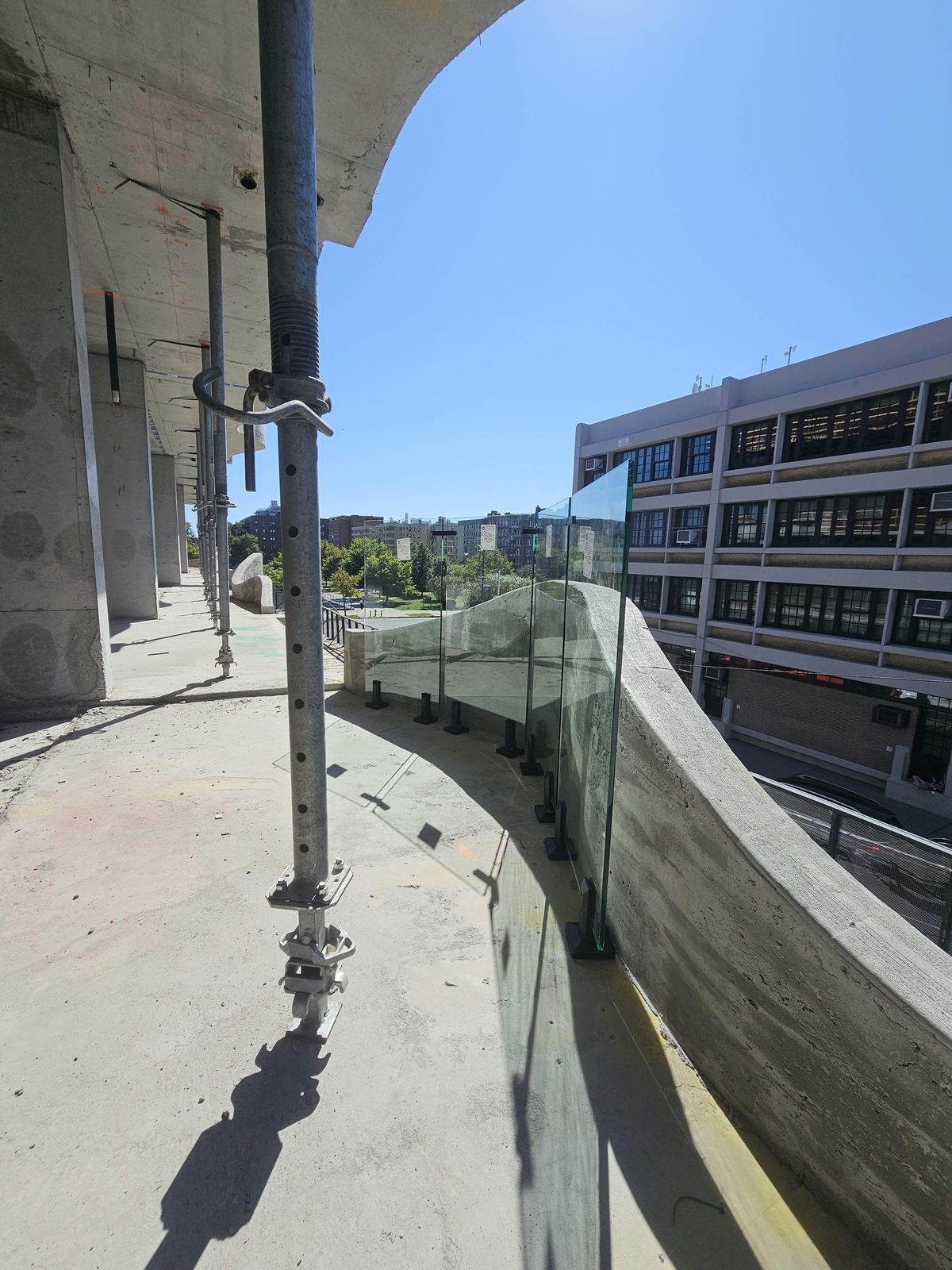 Mock-up of a spigot-mounted half-inch tempered glass railing following the wave-form concrete parapet on a balcony at 1505 Emmons Avenue, Sheepshead Bay