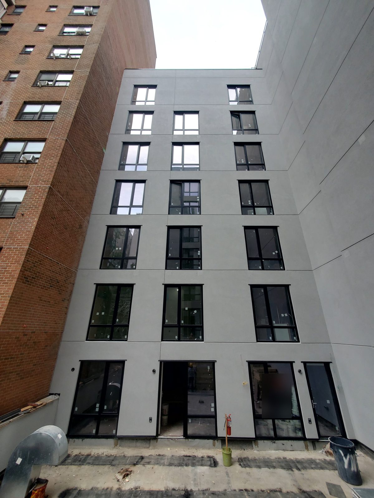 Rear stucco wall of 1526 Sedgwick Avenue, Bronx, with black windows on every floor and glazed doors at terrace level
