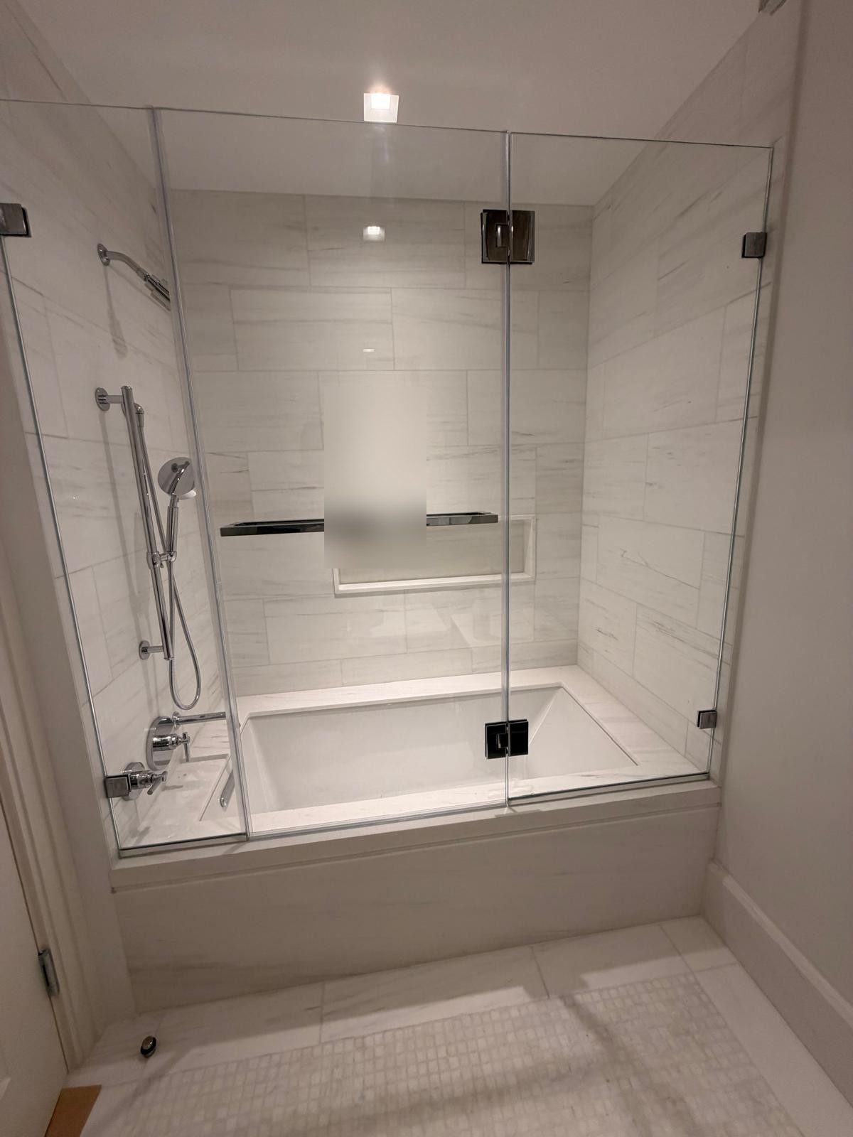 Custom frameless clear-glass shower door for a built-in bathtub at 16 5th Avenue, with a fixed panel at the plumbing end and a hinged door on polished chrome glass-to-glass hinges