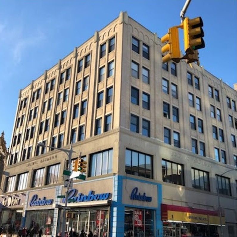 Multi-story brick and stone commercial building at 165-19 Jamaica Avenue, Jamaica, Queens, with dark aluminum double-hung windows on the upper floors