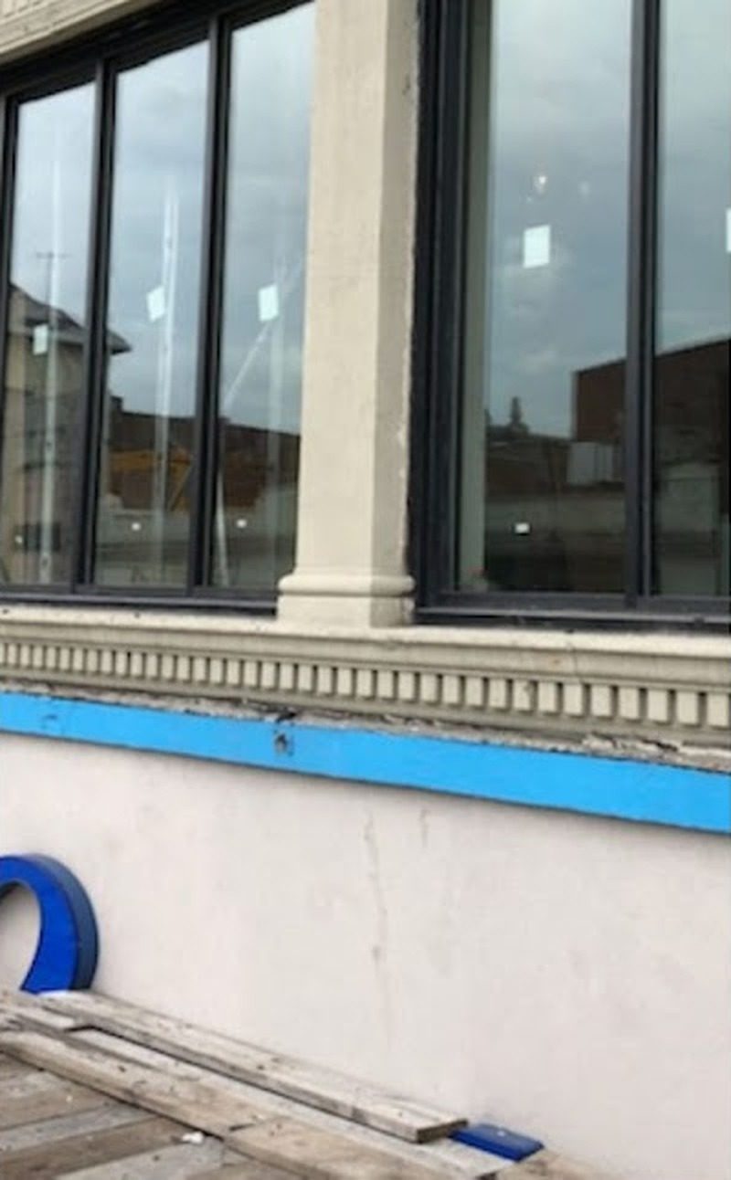 Storefront glazing in custom dark aluminum tubing beside a stone pier above a carved stone sill at 165-19 Jamaica Avenue, Jamaica, Queens