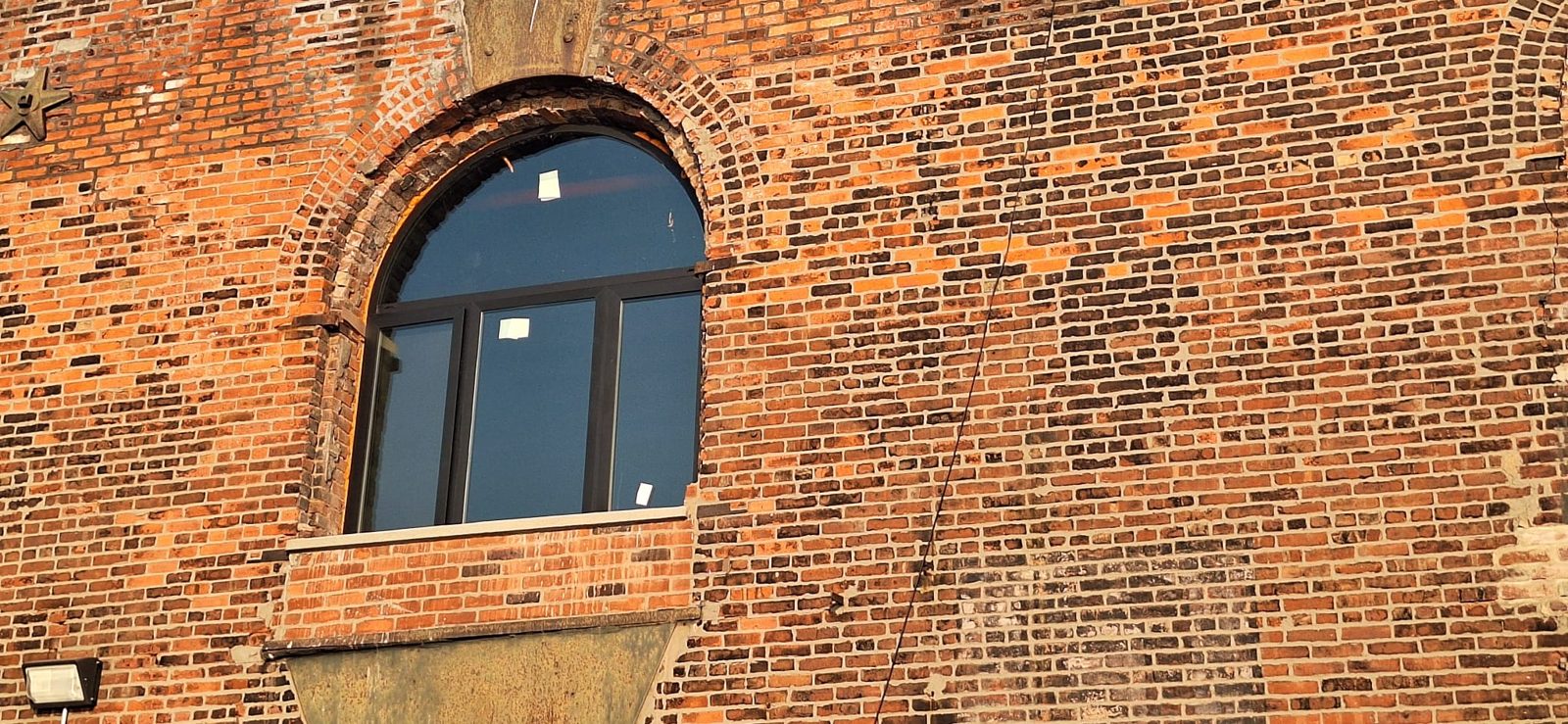 Custom arched black aluminium window with an arched fixed top lite over three lower lites in a round brick arch on a 19th-century warehouse at 185 Van Dyke Street, Red Hook, Brooklyn