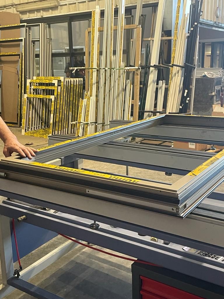 Alumil window frame being squared on the assembly bench with racked frames behind