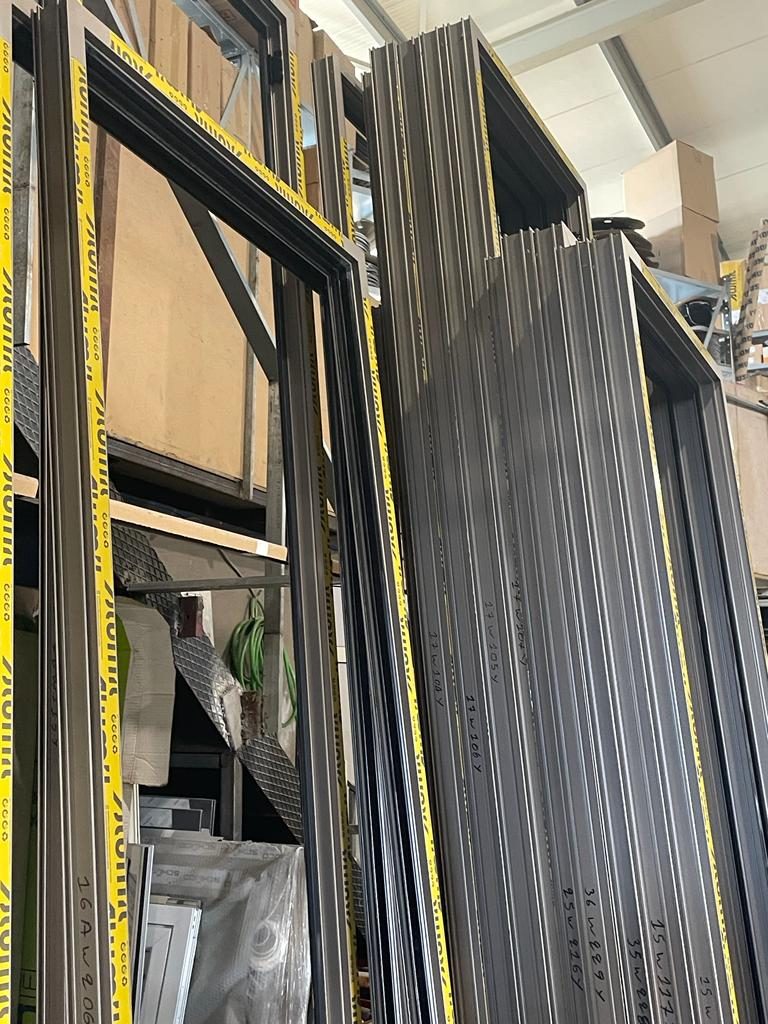 Stack of assembled Alumil frames in a dark bronze finish, each marked with its opening number