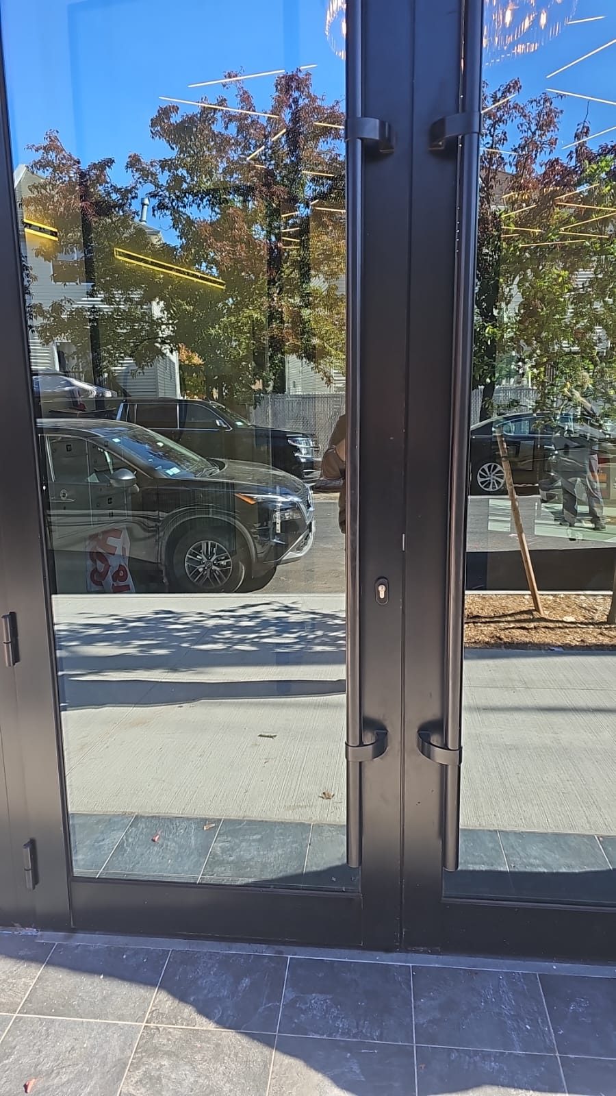 Custom 7-foot black offset ladder pull handles on a pair of aluminum entrance doors, with the lock cylinder accessible between the fixings