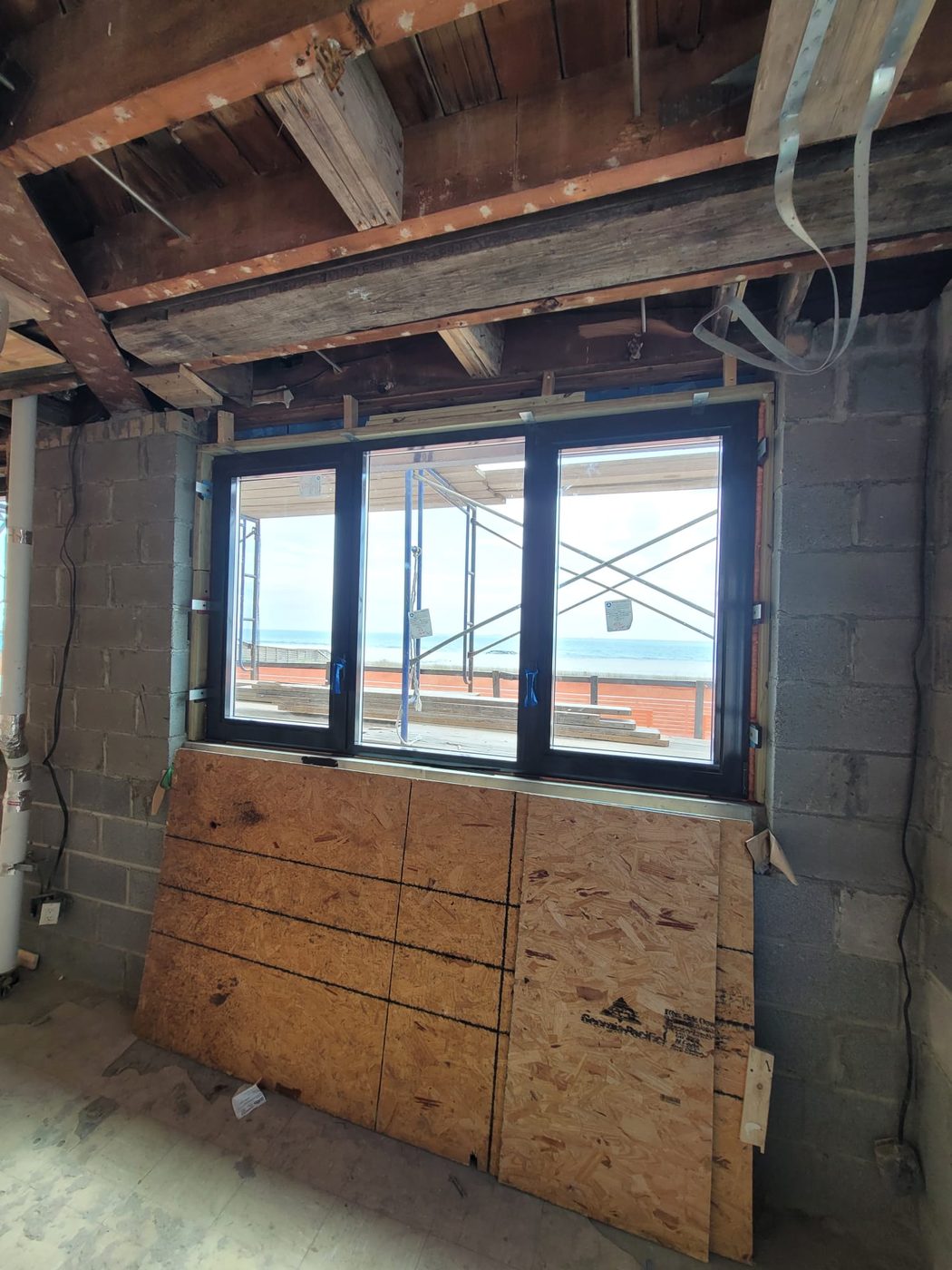 Alutech tilt-and-turn aluminum window being installed in a block wall at 25 Franklin Boulevard, with the beach and ocean through the glass