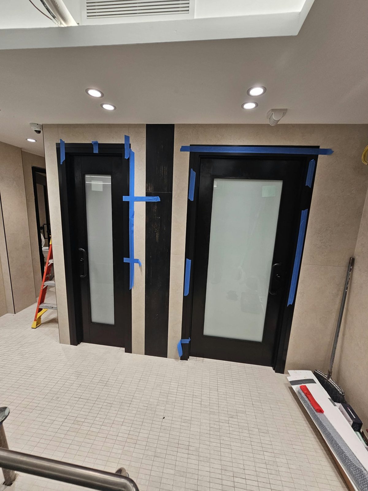 Two black anodized wide-stile aluminum doors with full-height white laminated glass, one narrow and one wide, set in porcelain-clad walls at 2555 Nostrand Avenue, Midwood, Brooklyn