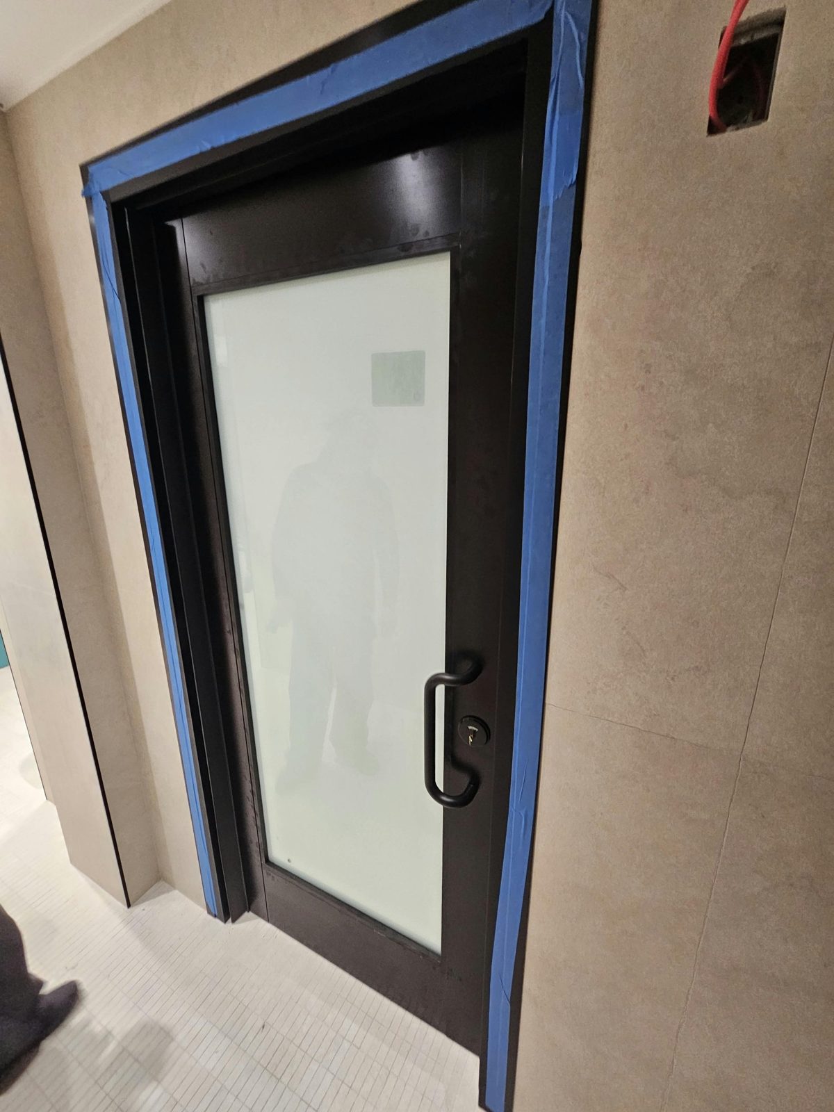Black wide-stile aluminum door with a white laminated glass lite, black offset pull handle and occupancy-indicator lock at 2555 Nostrand Avenue, Midwood