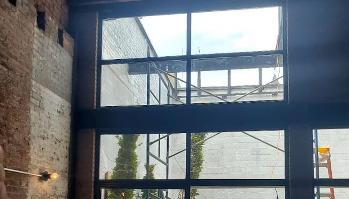 Tall gridded steel window wall with insulated glass beside exposed brick at 266 Bond Street, Brooklyn