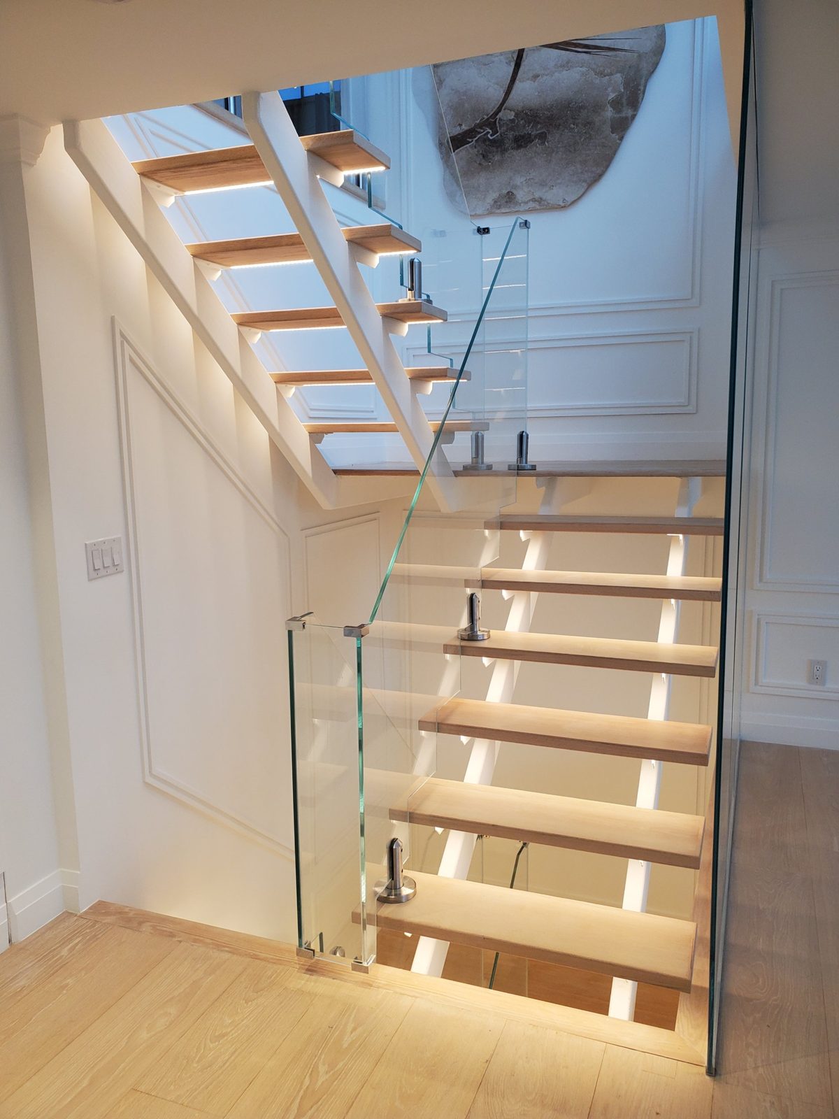 Frameless Starphire glass stair railing on stainless spigots beside an open-riser wood stair with LED-lit treads in a penthouse at 300 East 90th Street, Manhattan
