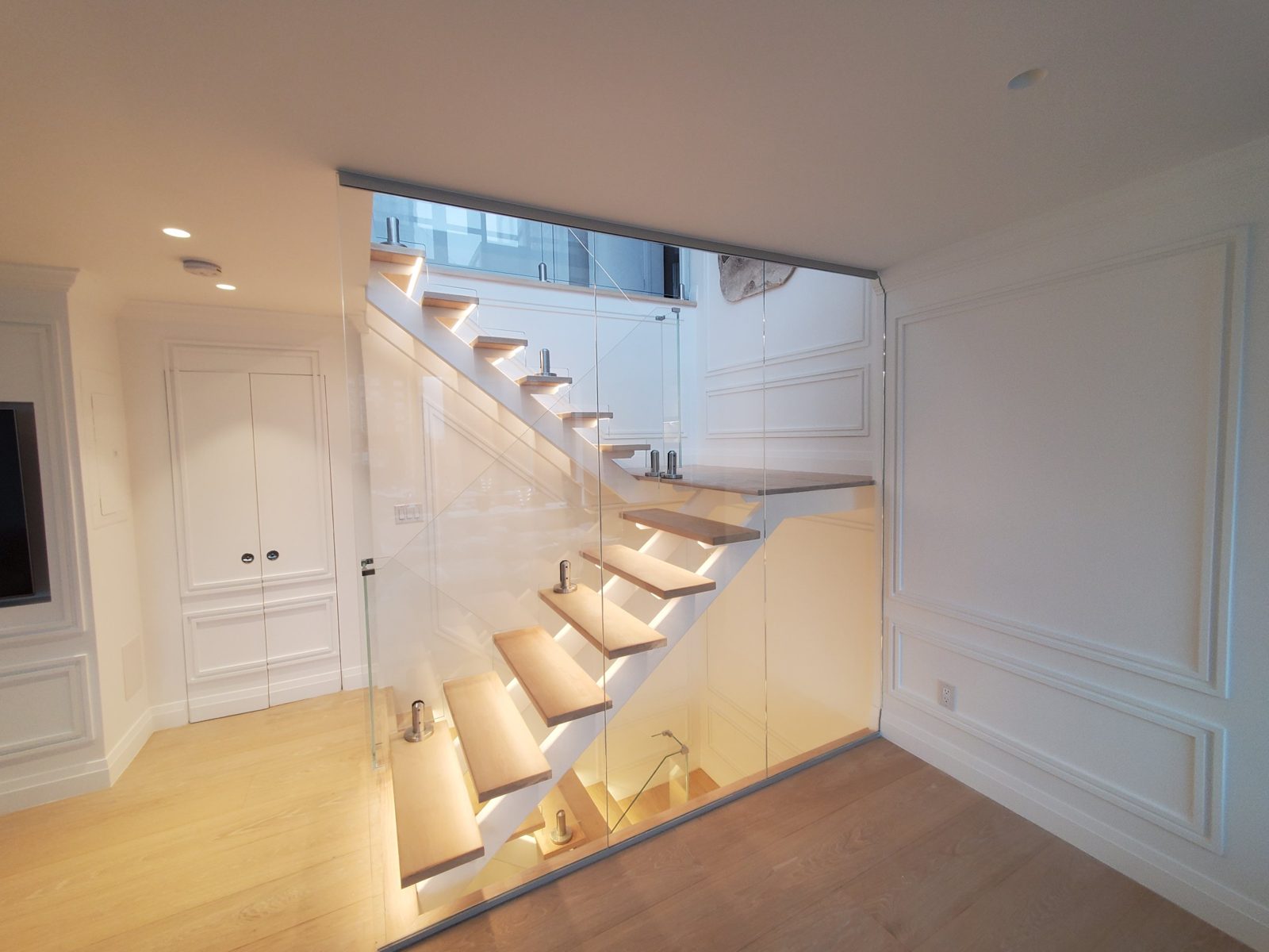 Floor-to-ceiling frameless glass wall beside the open-riser stair with LED-lit treads in a penthouse at 300 East 90th Street, Manhattan