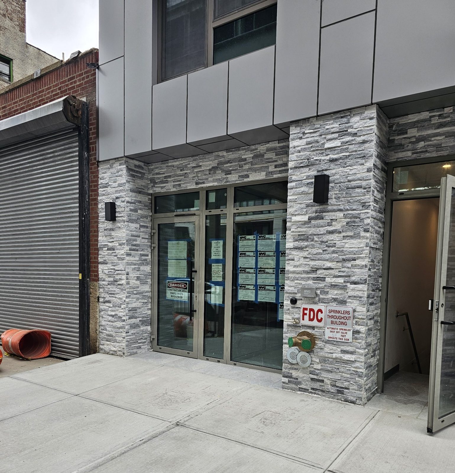 Custom gray aluminum storefront with a door, sidelite, fixed lite and transoms between split-face stone piers on a new building on 31st Street, Queens