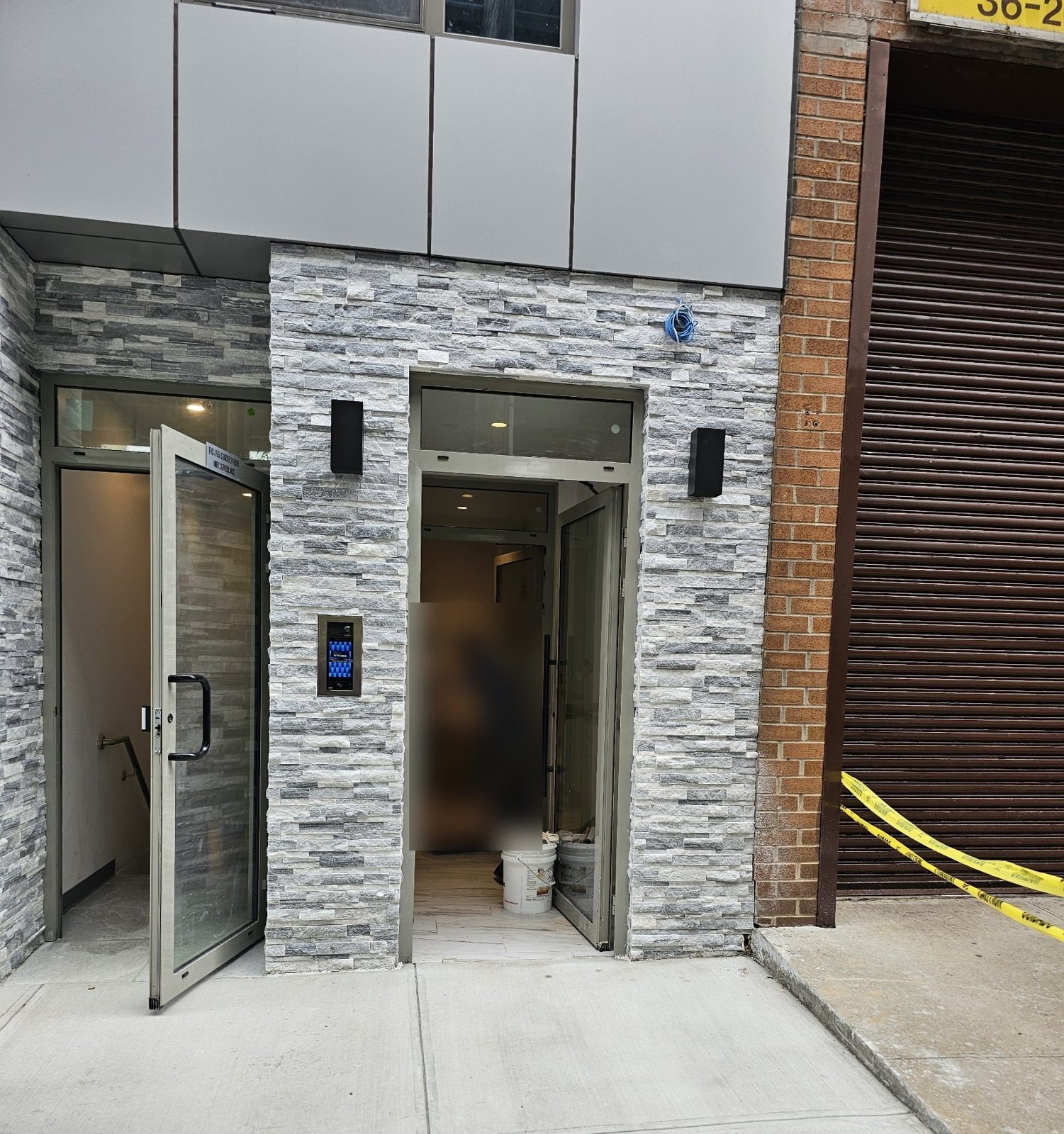 Lobby entrance and a second entrance door with transoms in custom gray aluminum framing on 31st Street, Queens, with an intercom panel set in the stone