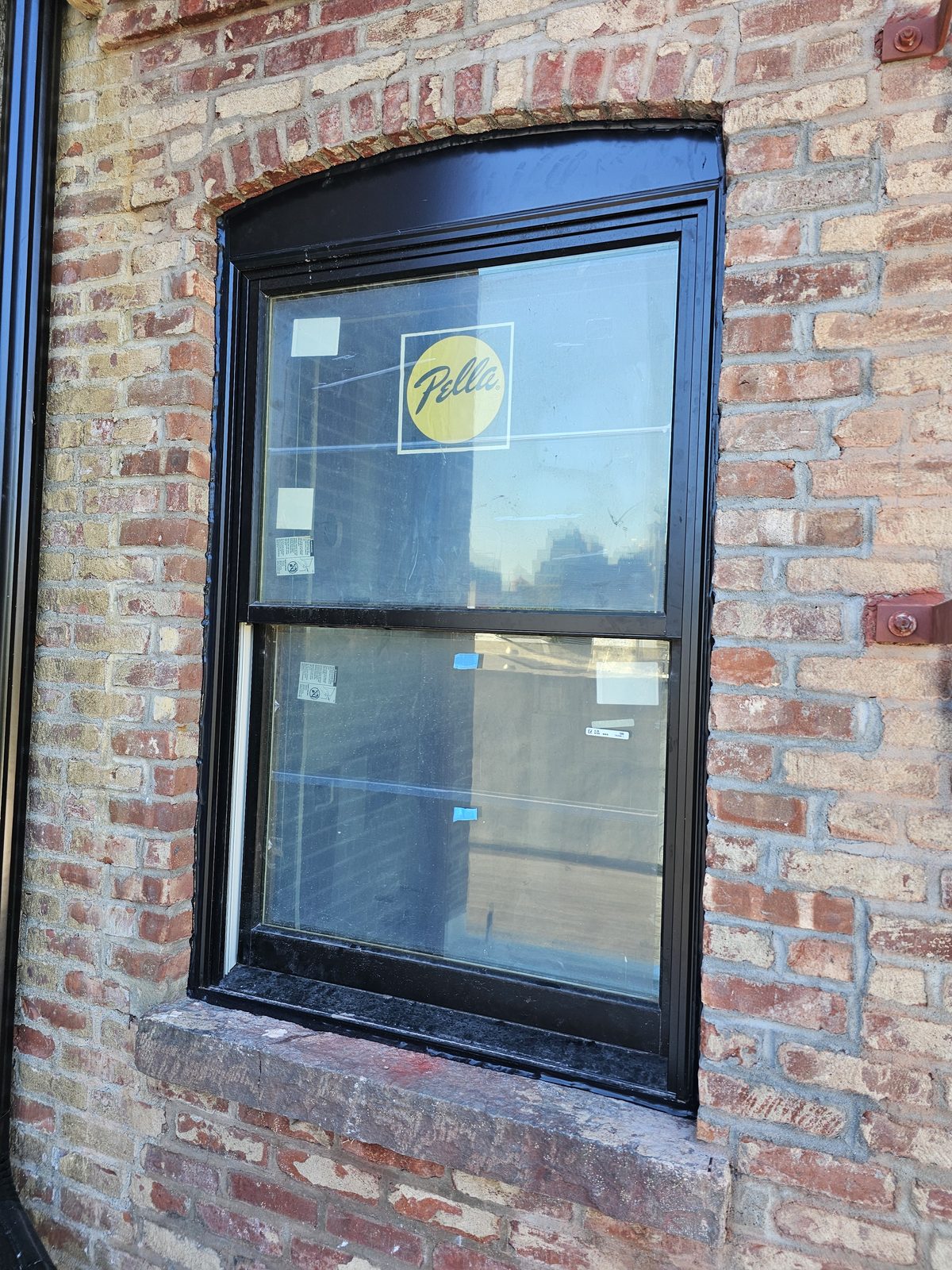 Black Pella double-hung window in an arched brick opening with a bluestone sill at 343 Hoyt Street, Carroll Gardens