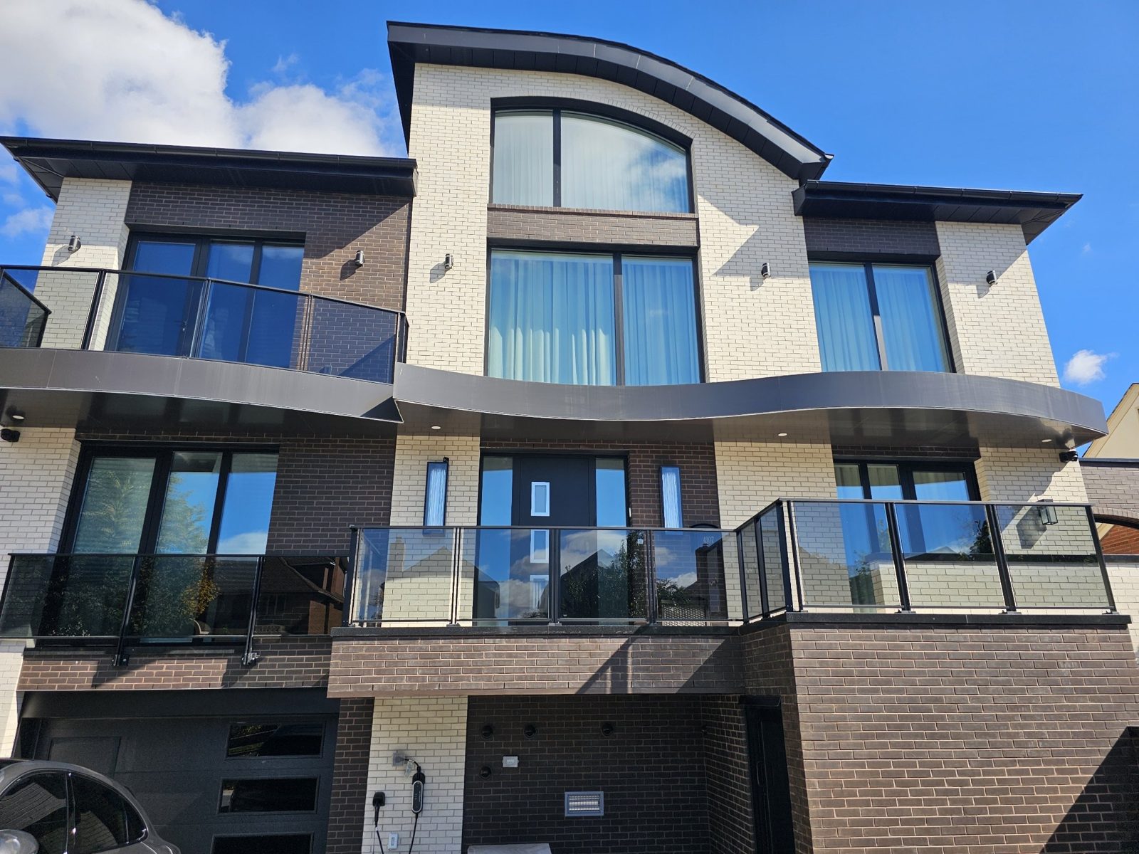 Front of the brick house at 4107 Ocean Avenue, Brooklyn, with dark Reynaers aluminum windows, an arched window under a curved roof, and glass balcony railings