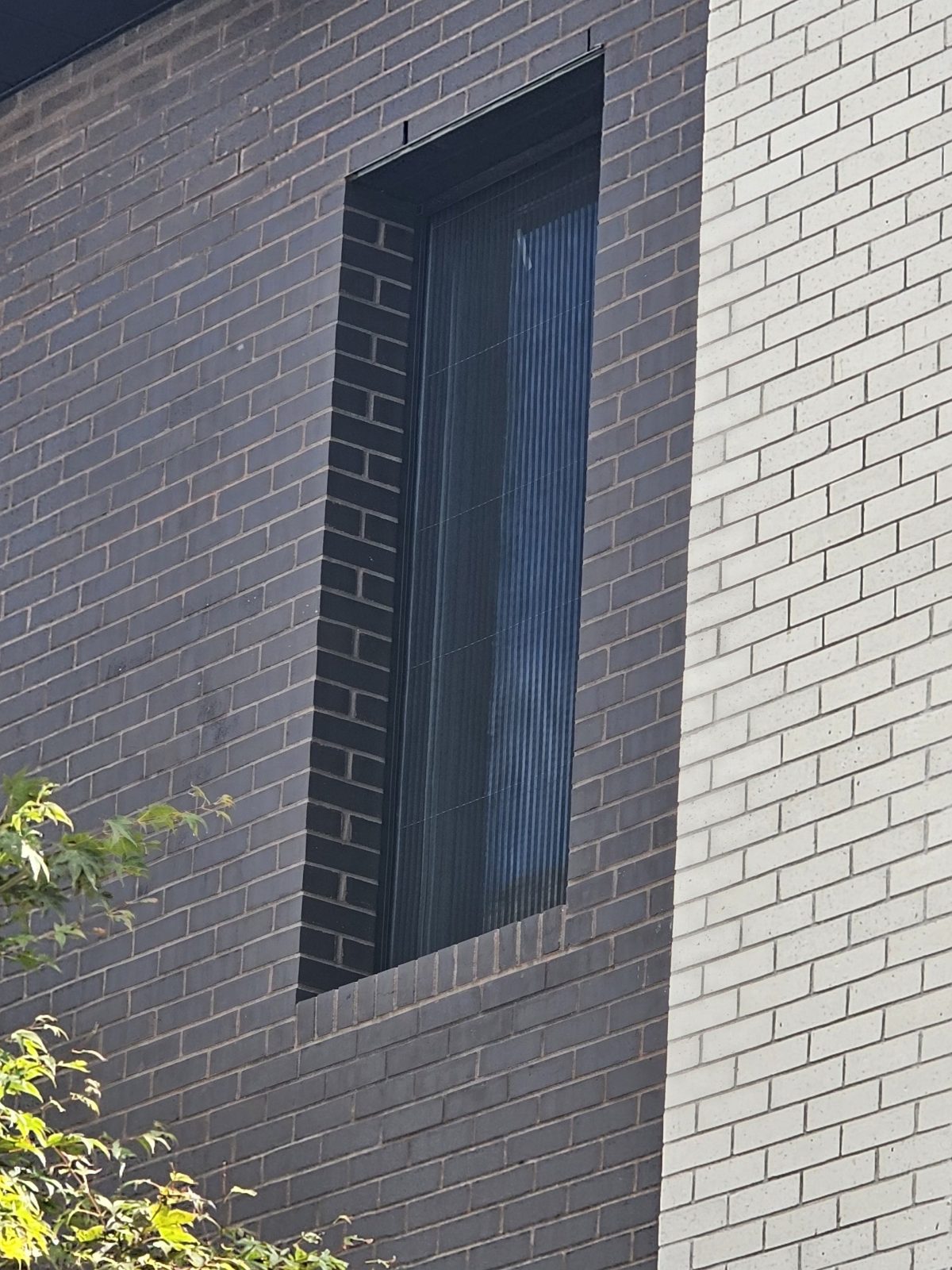 Tall narrow window with a pleated mosquito screen set in dark brick at 4107 Ocean Avenue, Brooklyn