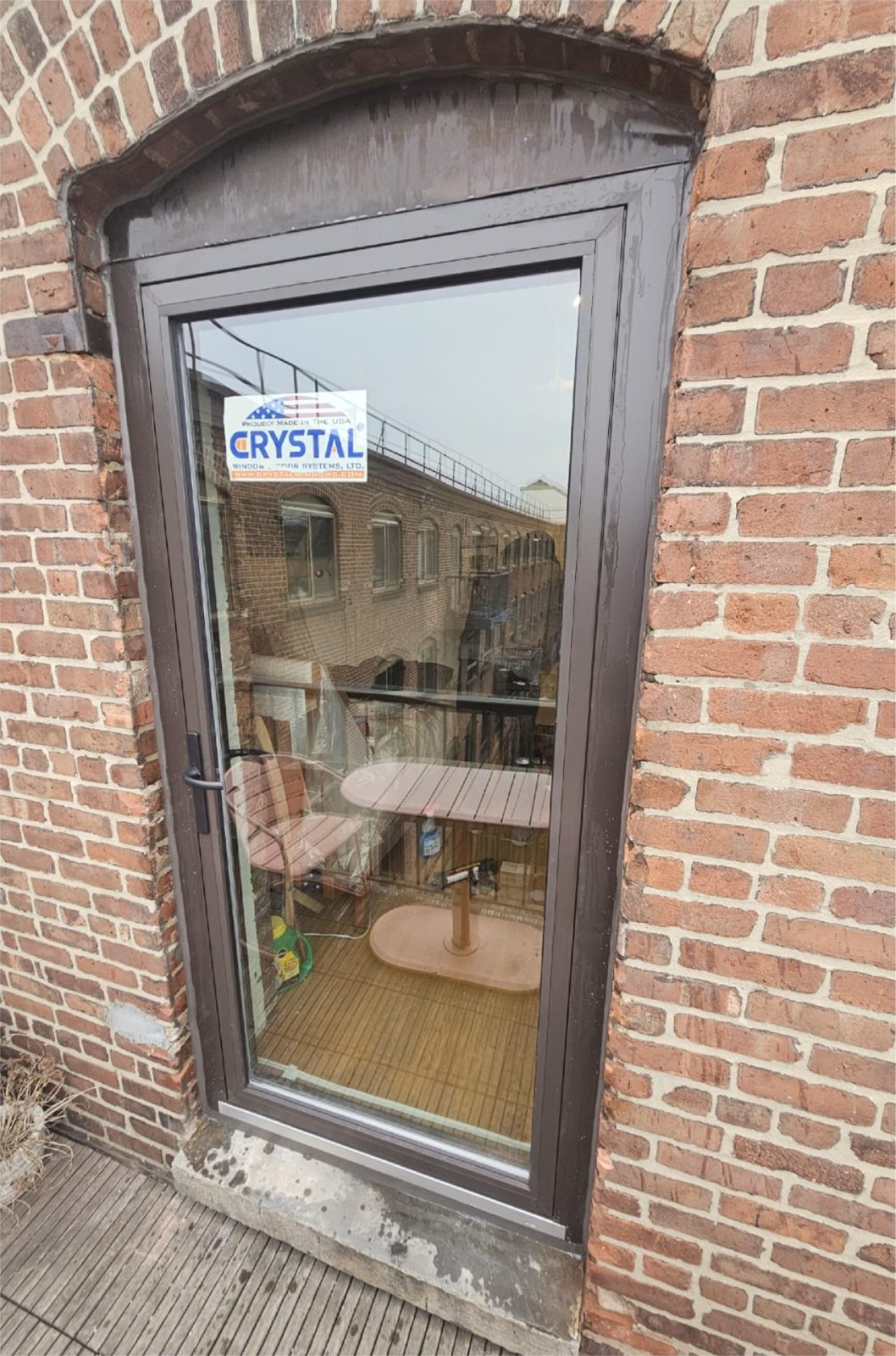 Dark bronze aluminium full-glass balcony door by Crystal Window & Door Systems in a segmental-arched brick opening at Ansonia Court, 420 12th Street, Park Slope, Brooklyn, seen from the private wood deck