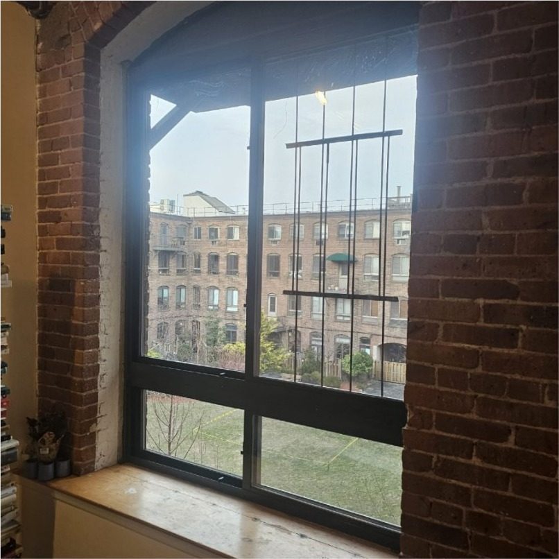 Crystal sliding aluminium window in dark bronze set in the arched brick opening of a converted factory loft at 420 12th Street, Park Slope, Brooklyn, looking across the courtyard