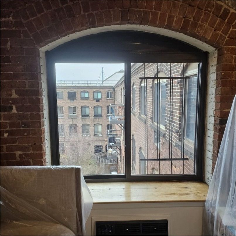Newly installed Crystal horizontal sliding aluminium window in an arched brick opening at 420 12th Street, Park Slope, Brooklyn, with dust sheets over the furniture on installation day