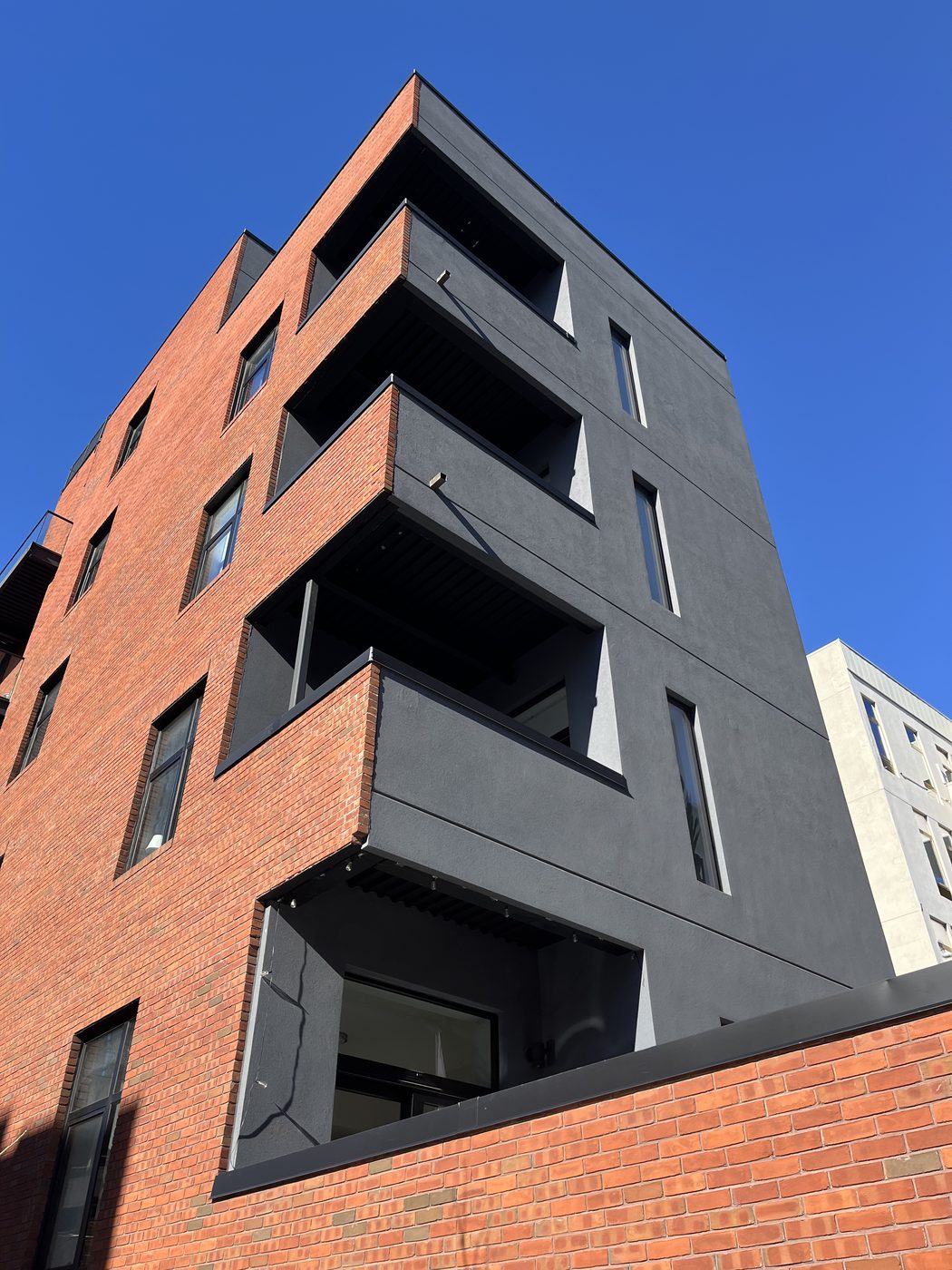 Dark side elevation of 5-13 47th Road, Long Island City, with tall narrow aluminum windows and balconies with glass railings