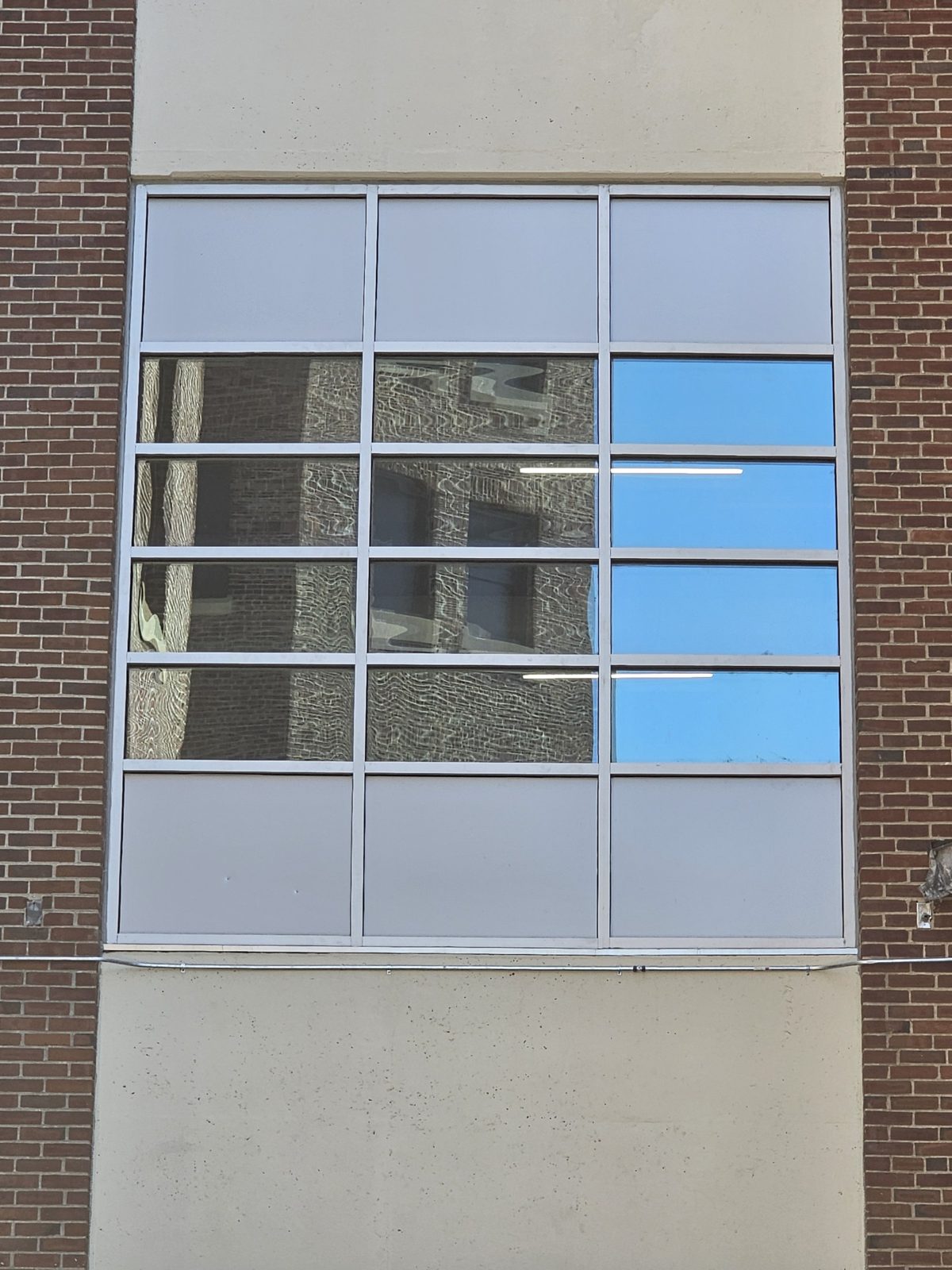 Close view of a fixed thermally broken aluminium window-wall bay, three modules wide, with horizontal glass lites between top and bottom rows of solid panels, at 60 East Haines Street, Germantown