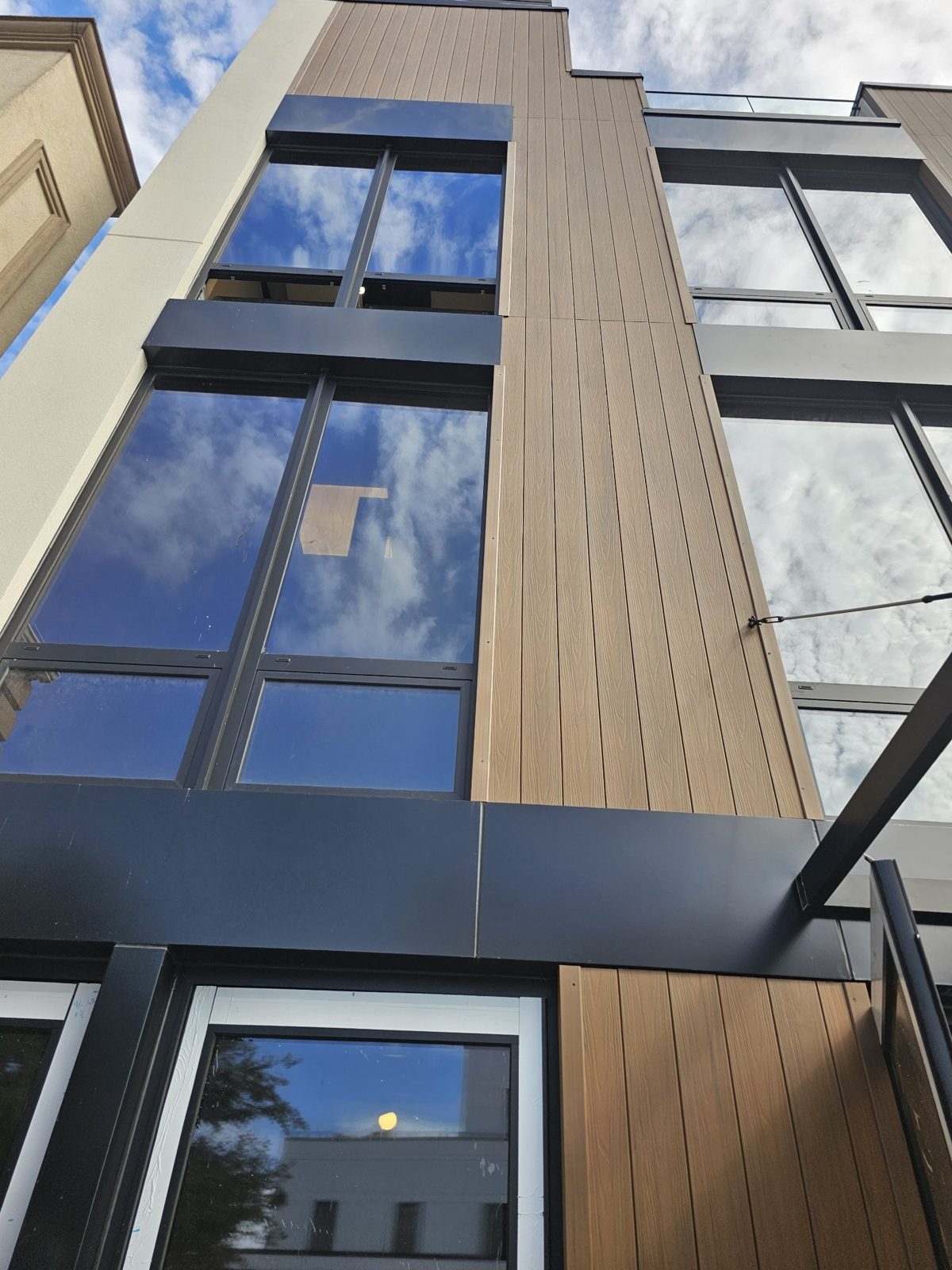 Looking up the facade at 75-65 186th Street, Queens: wood-look rigid panel band between window columns and black ACM bands at each floor
