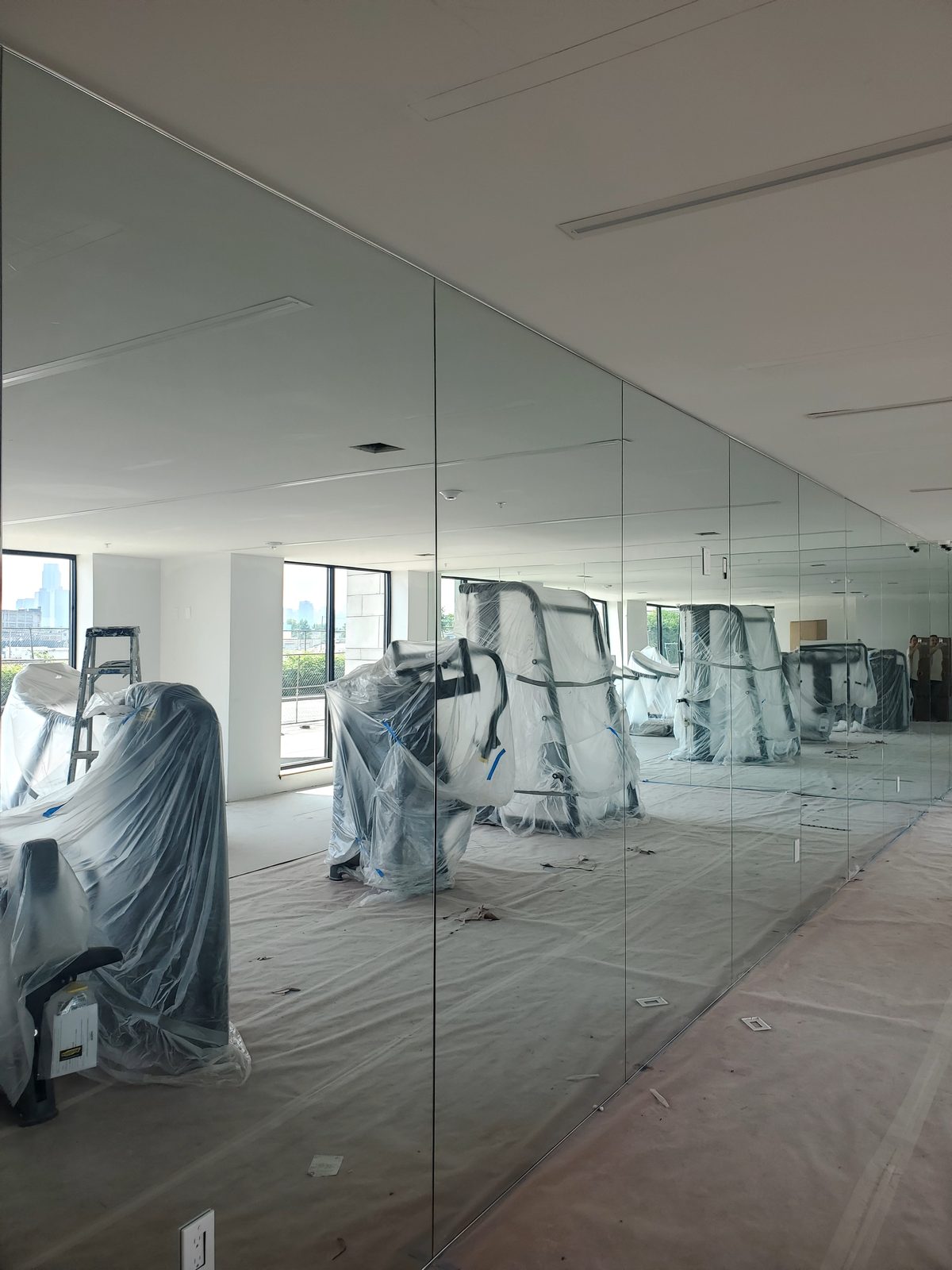 Full-height mirror wall of butt-jointed panels along the fitness center at 829 Garfield Avenue, Jersey City, with equipment still wrapped and skyline windows beyond