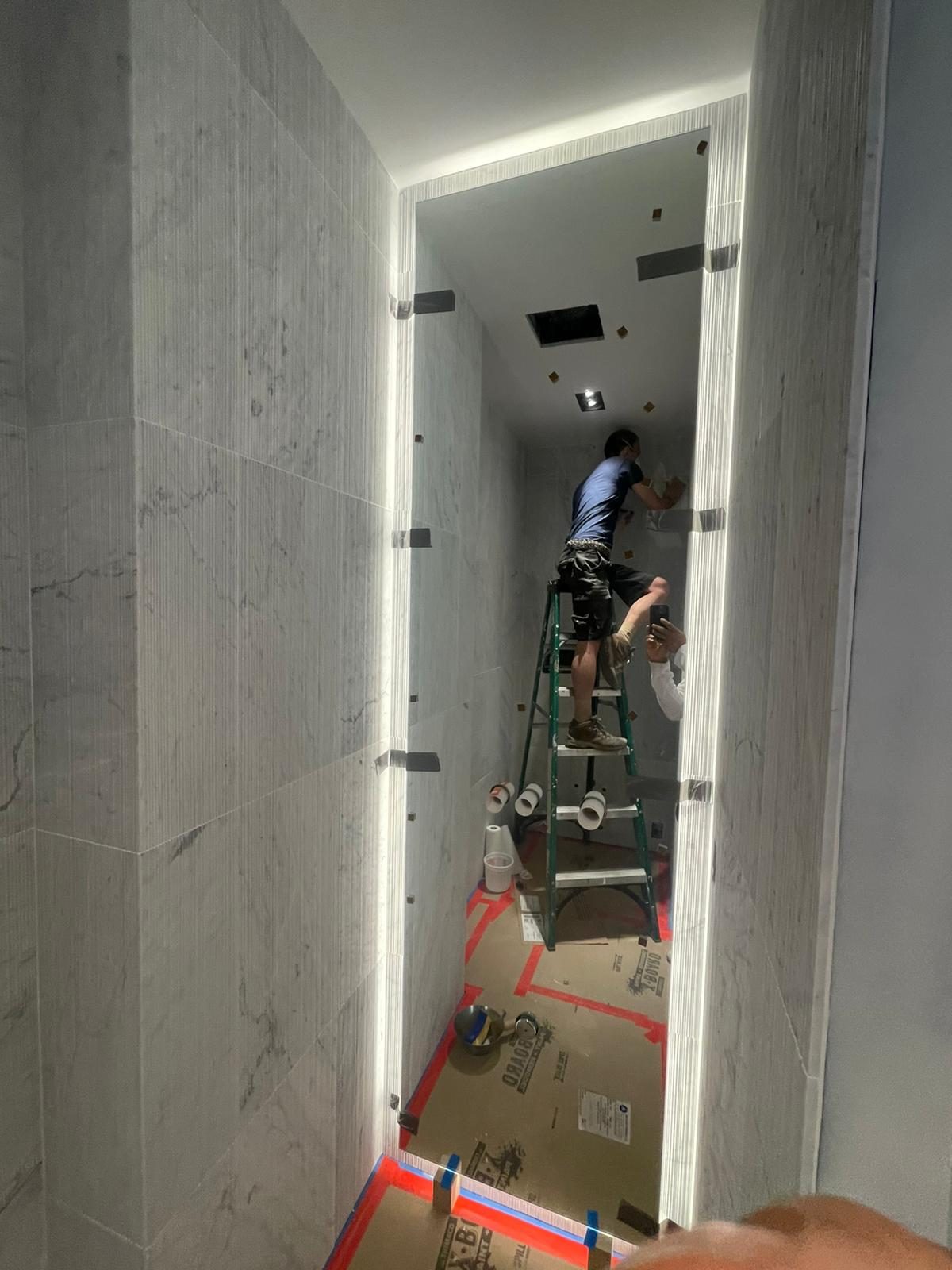 Full-height custom LED mirror being installed in a narrow marble-clad powder room at 95 Greene Street, SoHo, temporary clips holding the glass
