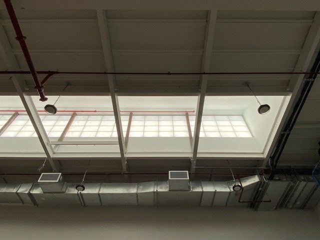 Kalwall translucent panels glowing behind the roof framing inside 96 Ingraham Street, Brooklyn