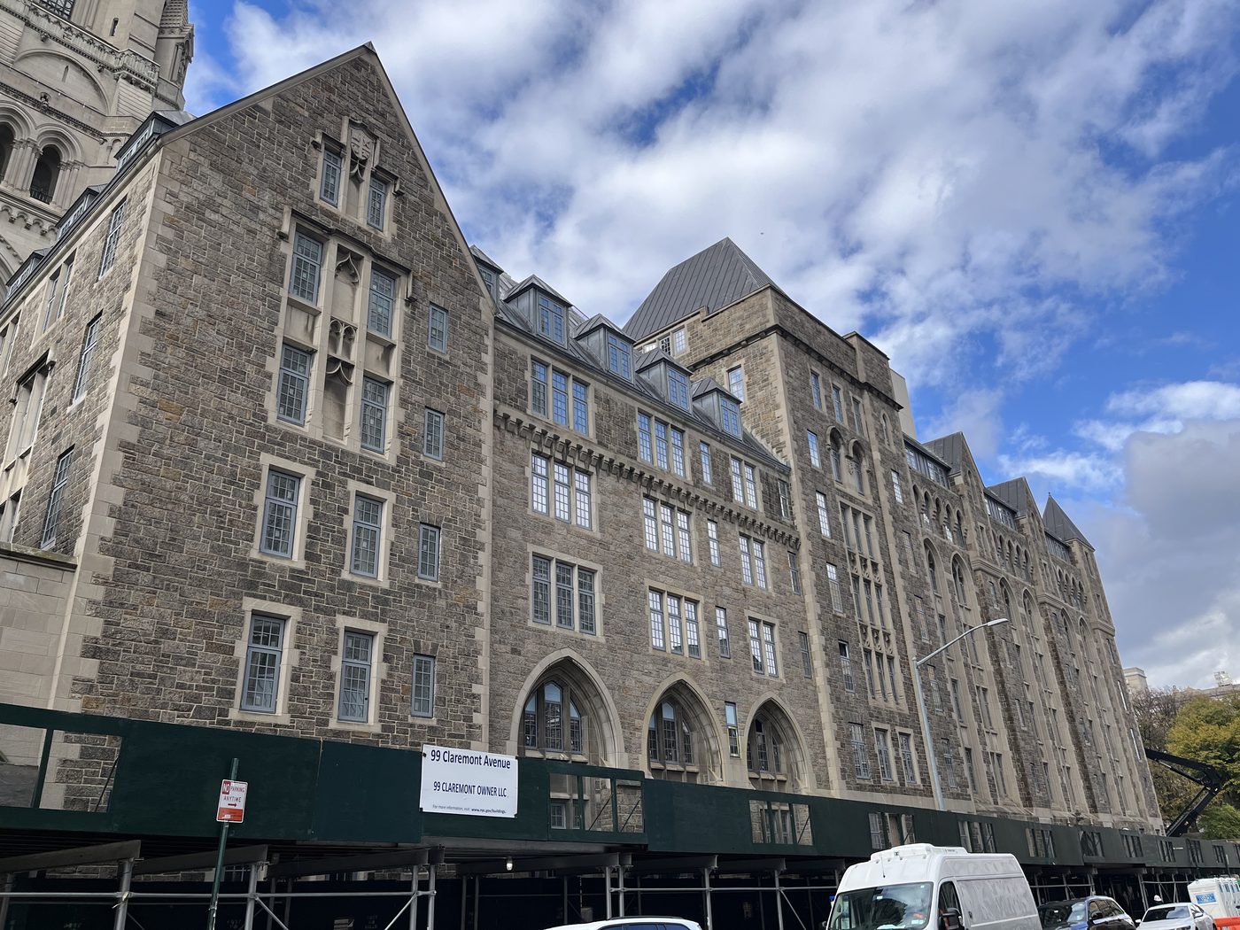 Gabled front facade of 99 Claremont Avenue, Manhattan, with new aluminum windows and the site sign on the sidewalk shed