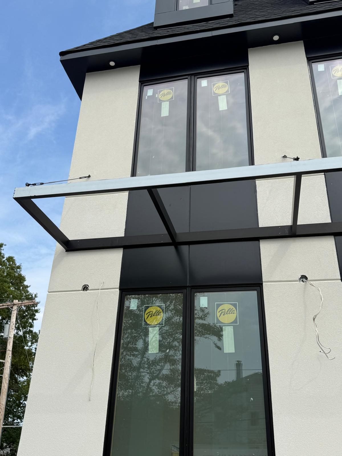 Cantilevered steel entrance canopy with cable stays under the black soffit at a new custom house in Woodmere, Pella windows above