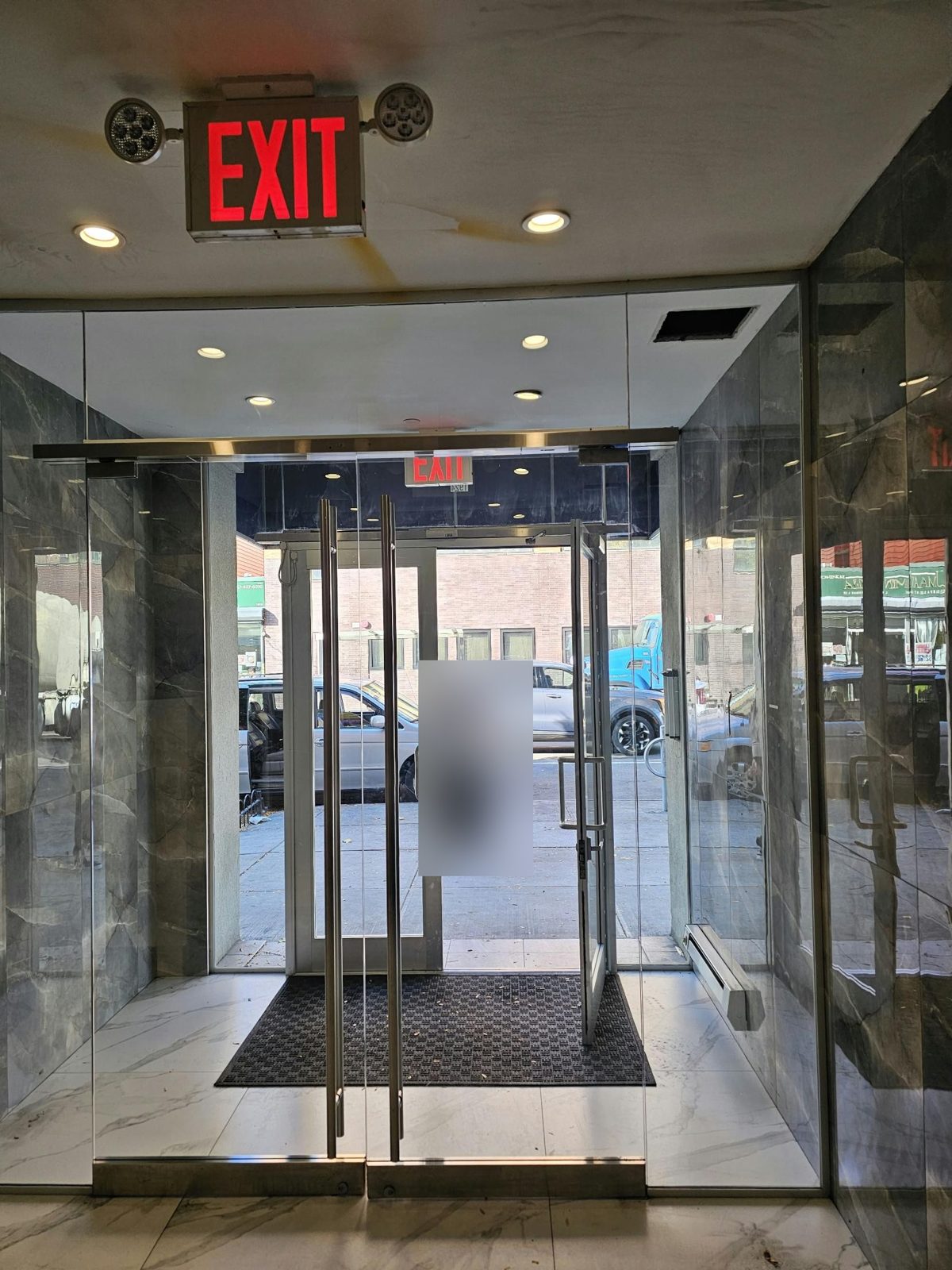 Pair of frameless herculite glass lobby doors with full-height tubular pulls in a marble vestibule at Avenue M and Ocean Avenue, Brooklyn, after realignment