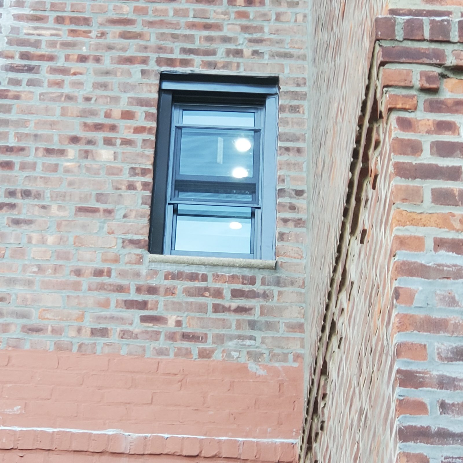 Small dark-framed double-hung replacement window in a brick wall, Brighton Beach, Brooklyn