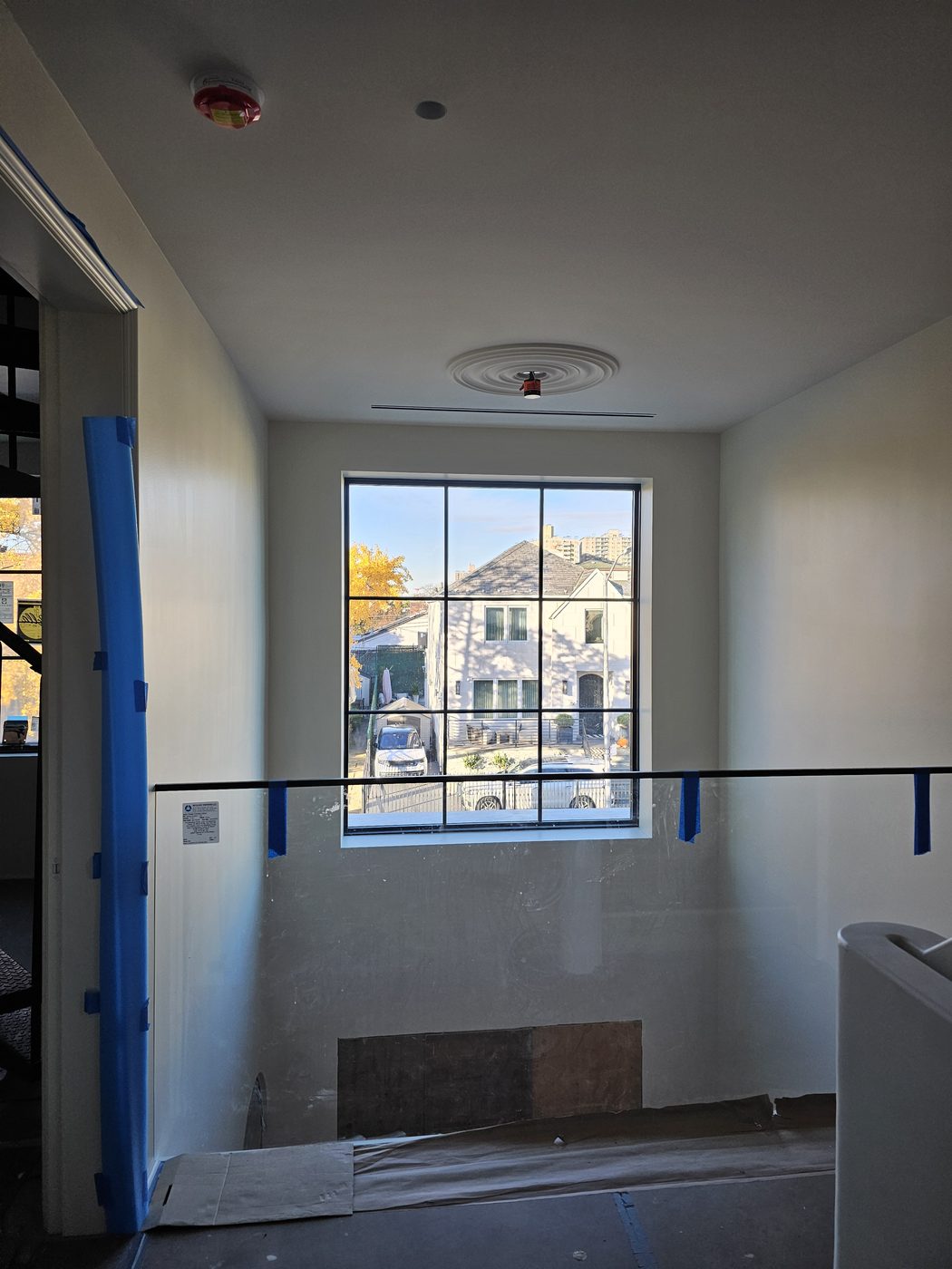 Stair hall of the Manhattan Beach house with a single large divided-lite window looking onto the street