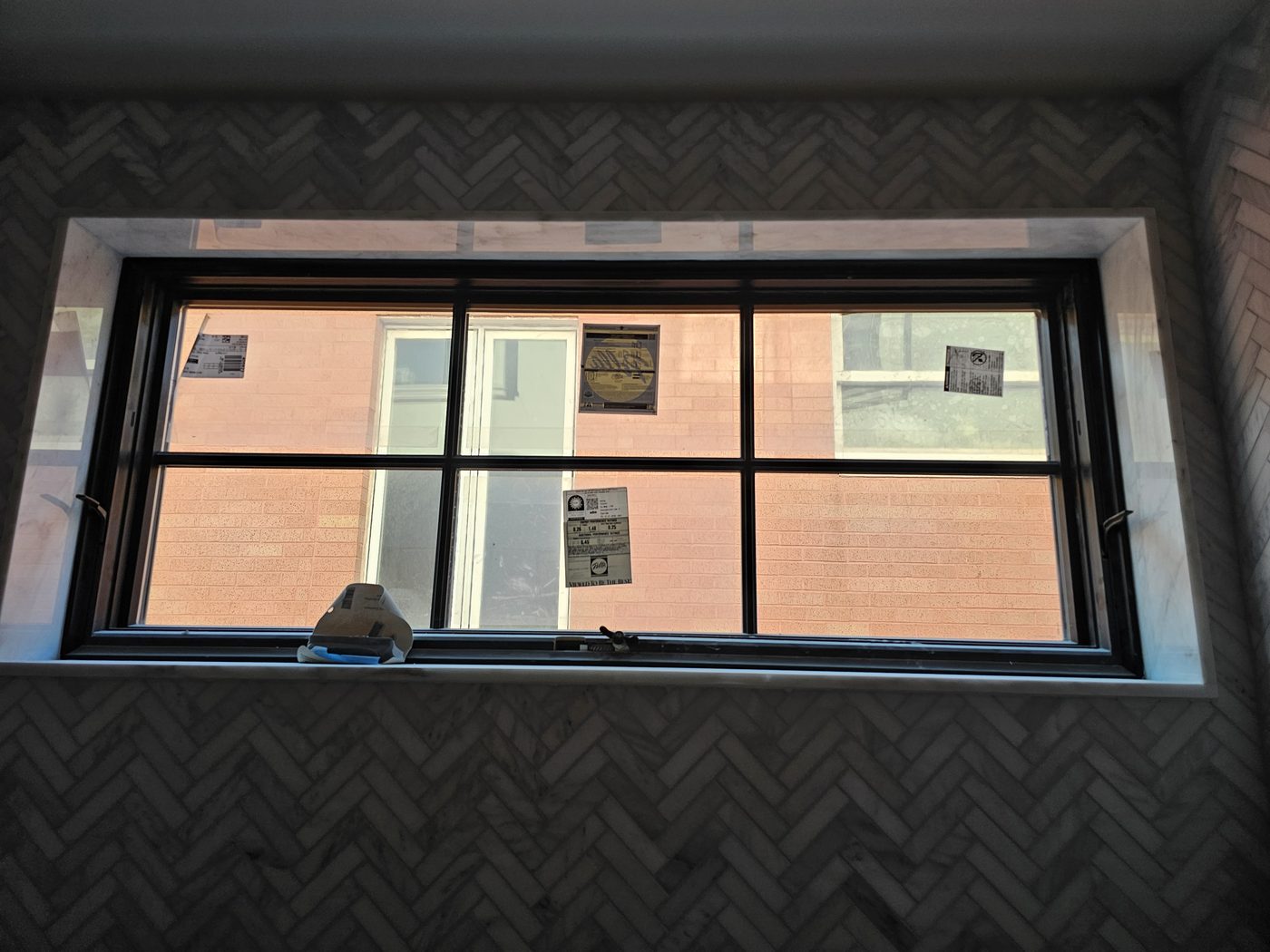Wide Pella window set in a marble surround with herringbone tile in a bathroom of the Manhattan Beach house