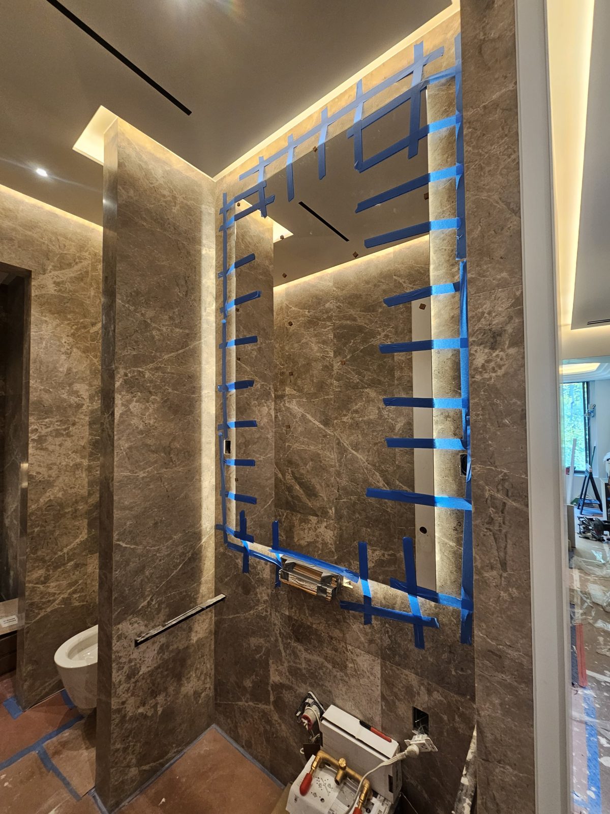 Low-iron LED backlit mirror being installed on a grey marble wall in a powder room on East 18th Street, Manhattan, with the LED halo glowing behind the taped glass
