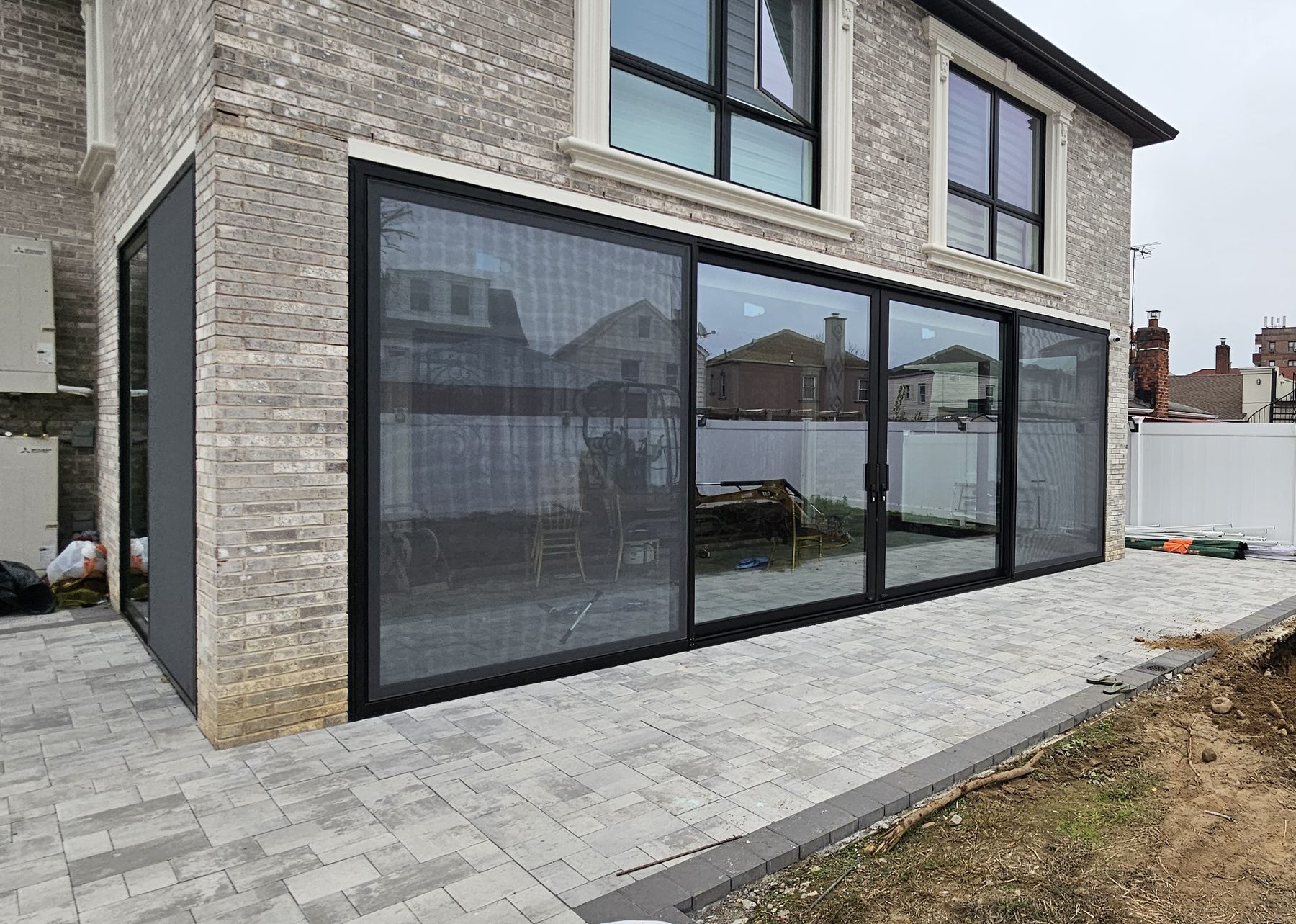 The full elevation: multi-panel sliding doors with integrated mosquito screens, opening onto the paved terrace &mdash; Jamaica Estates, Queens
