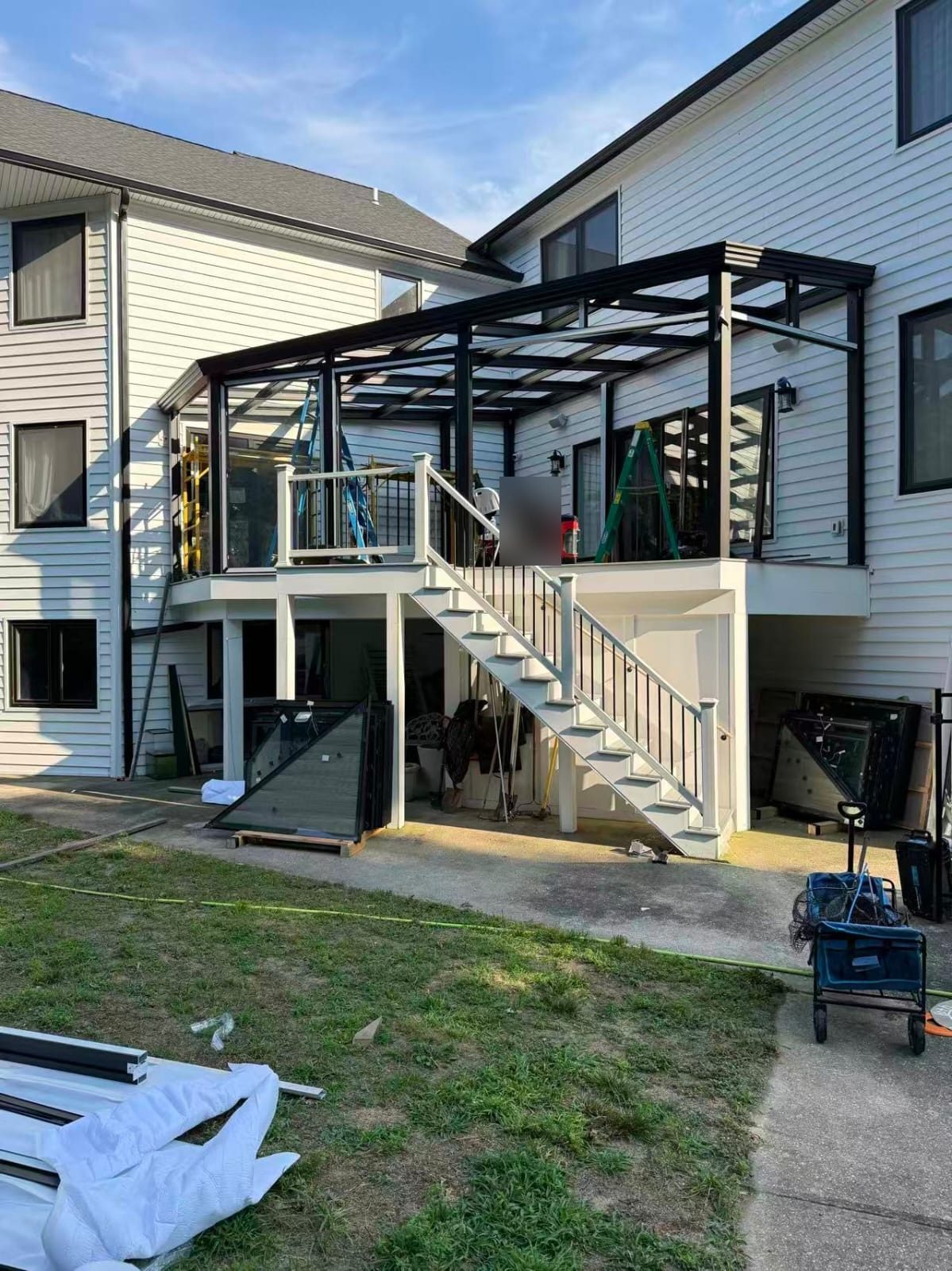 Black aluminum sunroom frame and roof structure on the raised deck during installation in Manalapan, NJ, with glass units stacked below