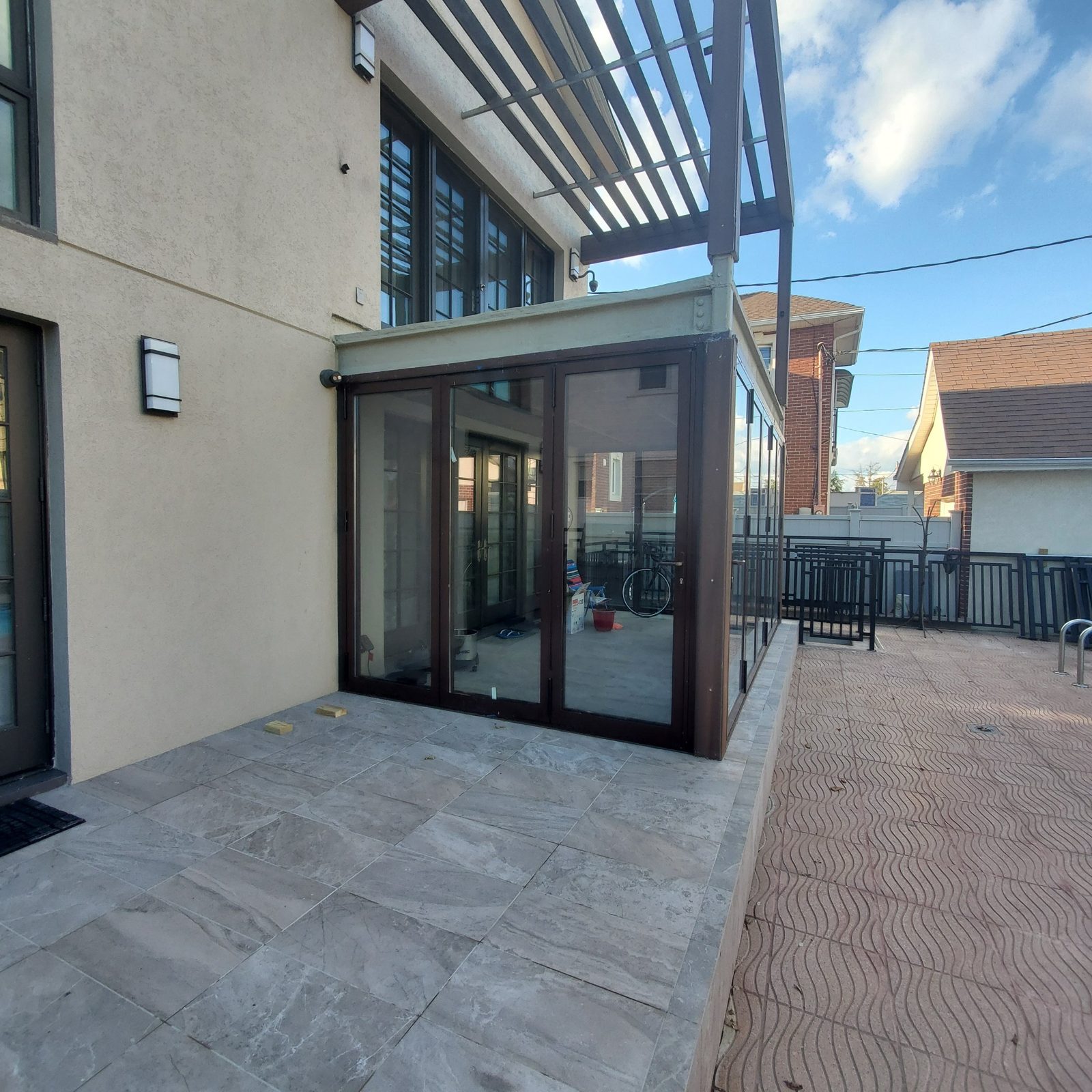 Sunroom enclosed with brown aluminum bifold glass doors on the patio of a house in Manhattan Beach, Brooklyn