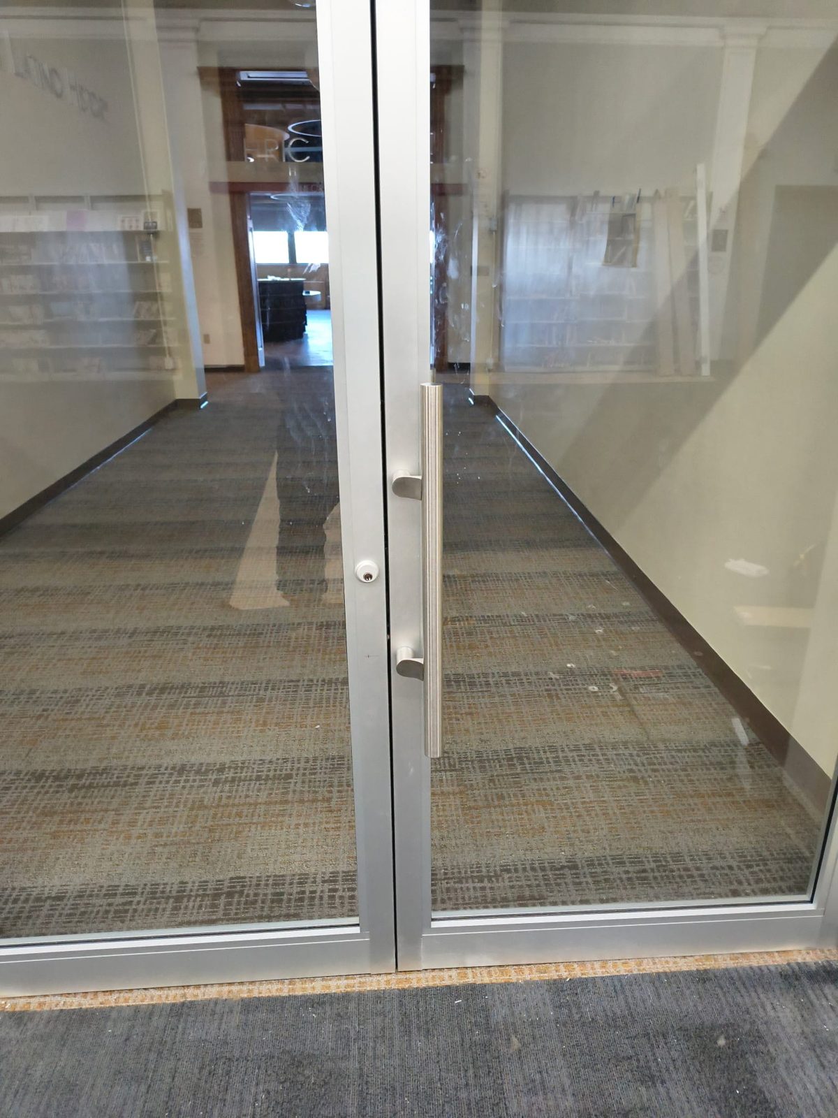 Detail of a pair of aluminum-framed glass doors with bar pulls and a cylinder lock, Newark Public Library, Newark NJ